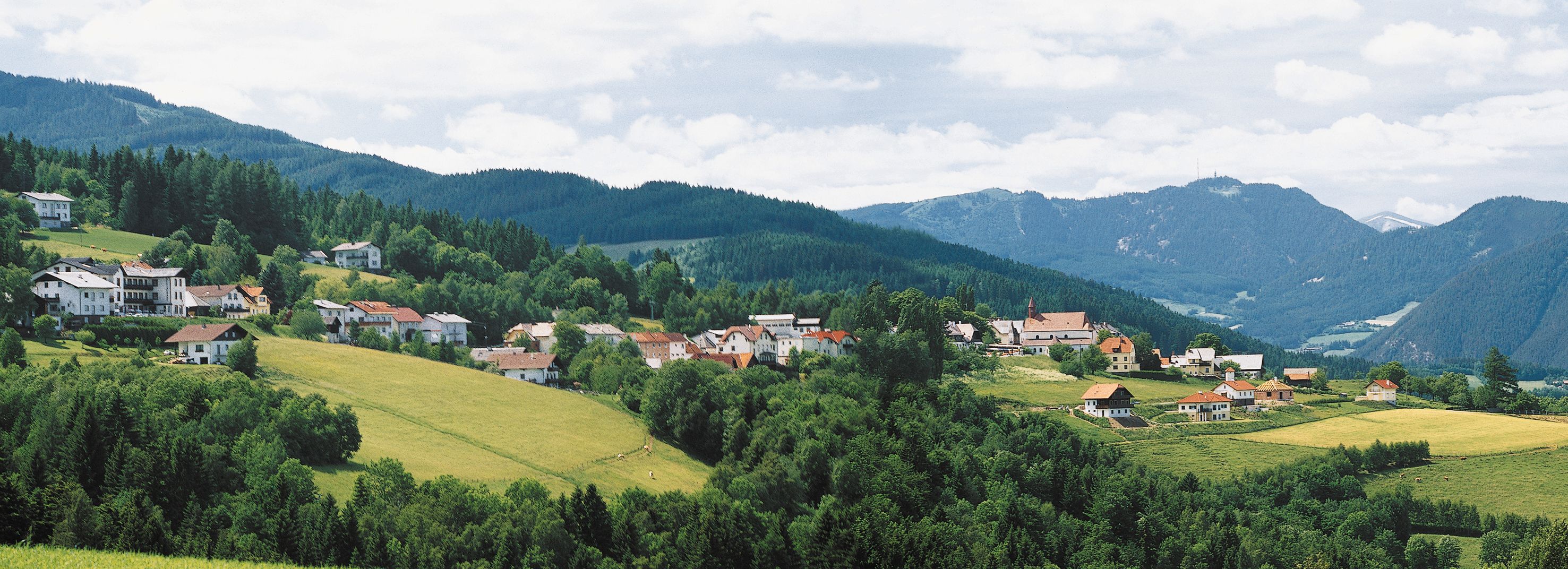 Panorama of St. Corona am Wechsel with green hills and mountains in the background.