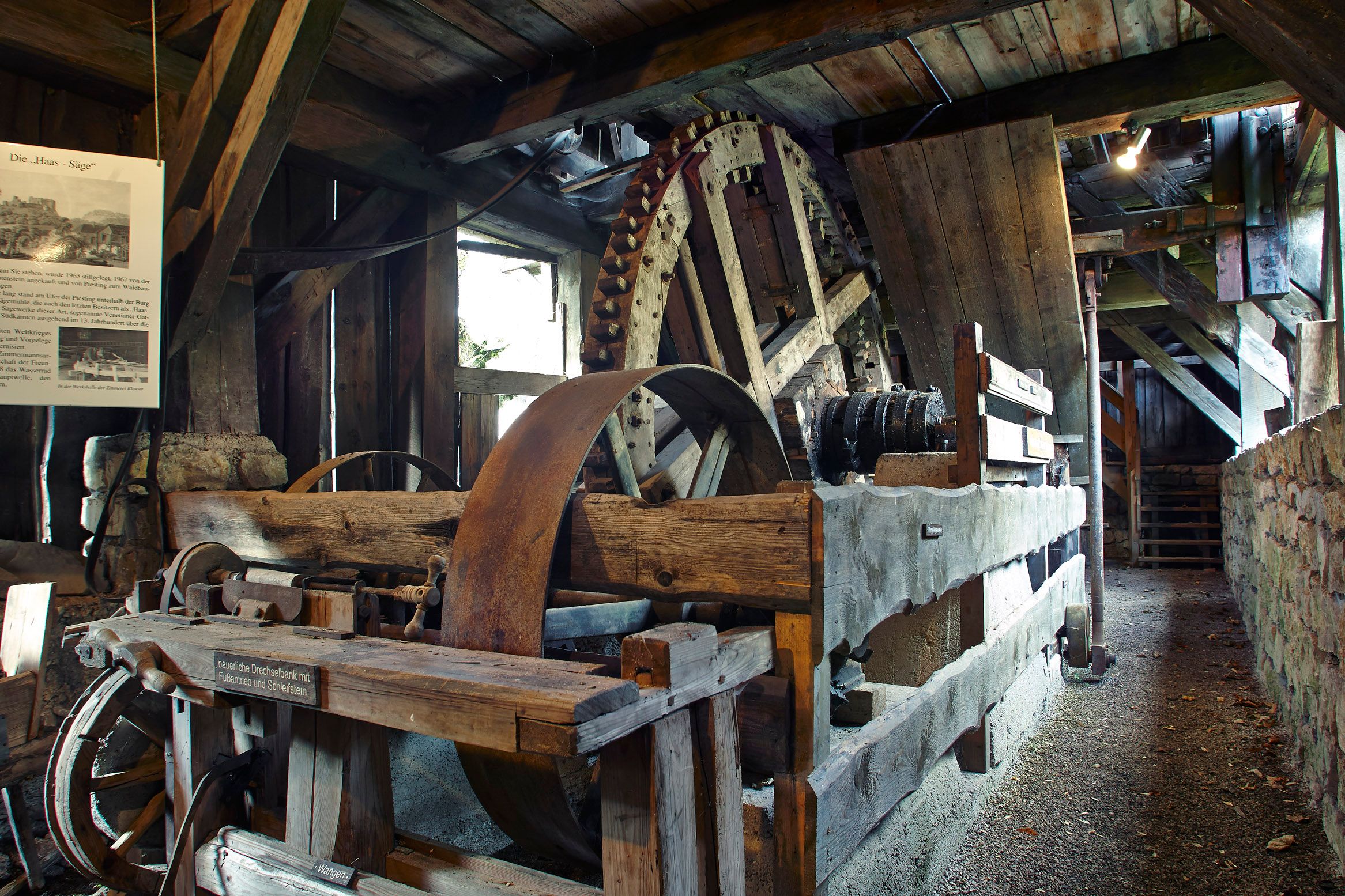Interior view of a historic sawmill with large wooden cogwheels and wooden beams.