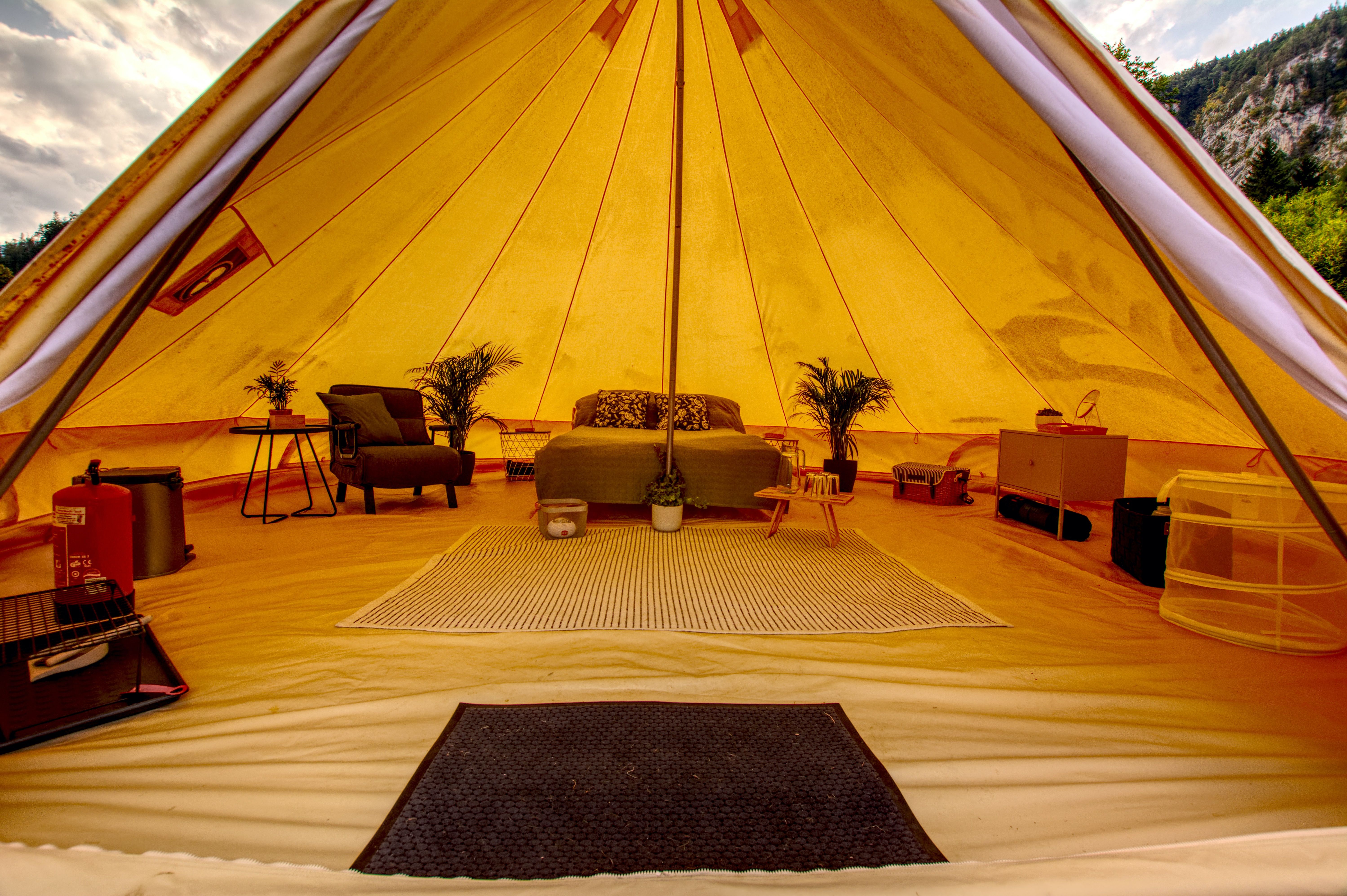 Interior view of a luxury glamping tent with bed, plants and furniture.