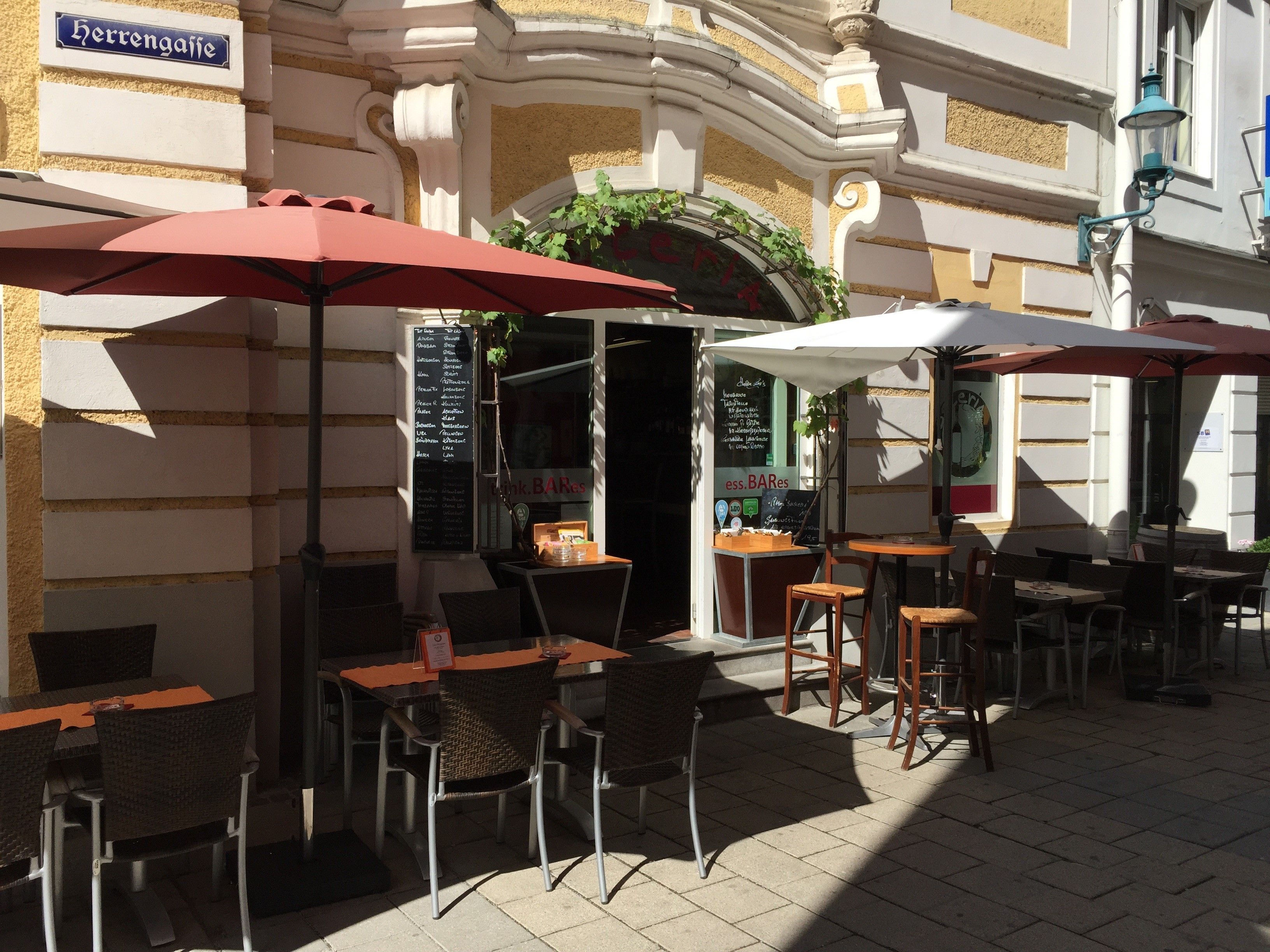 Outdoor area of a restaurant with tables, chairs and parasols in a sunny alley.