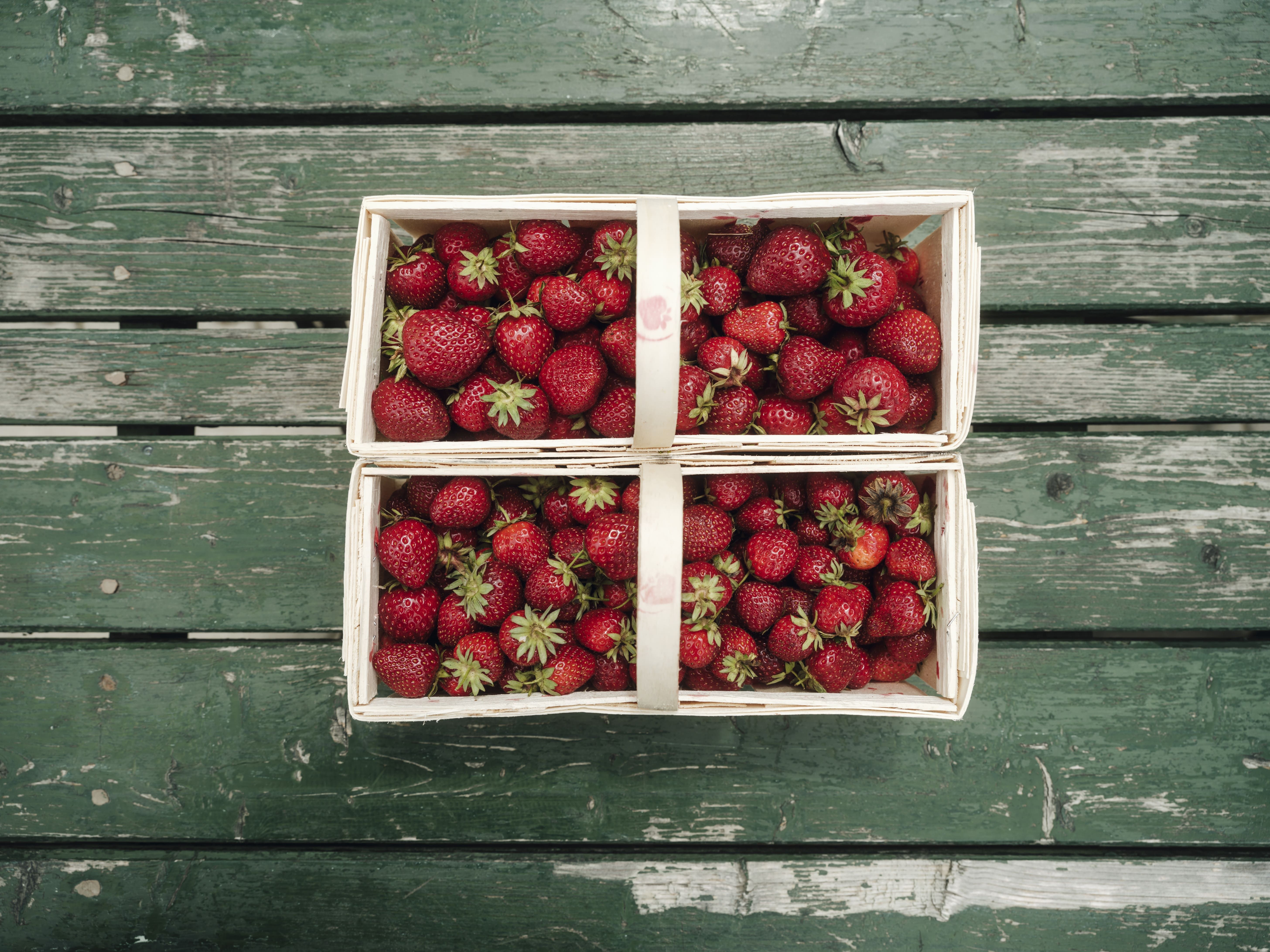 Two baskets of fresh strawberries on a green wooden table.