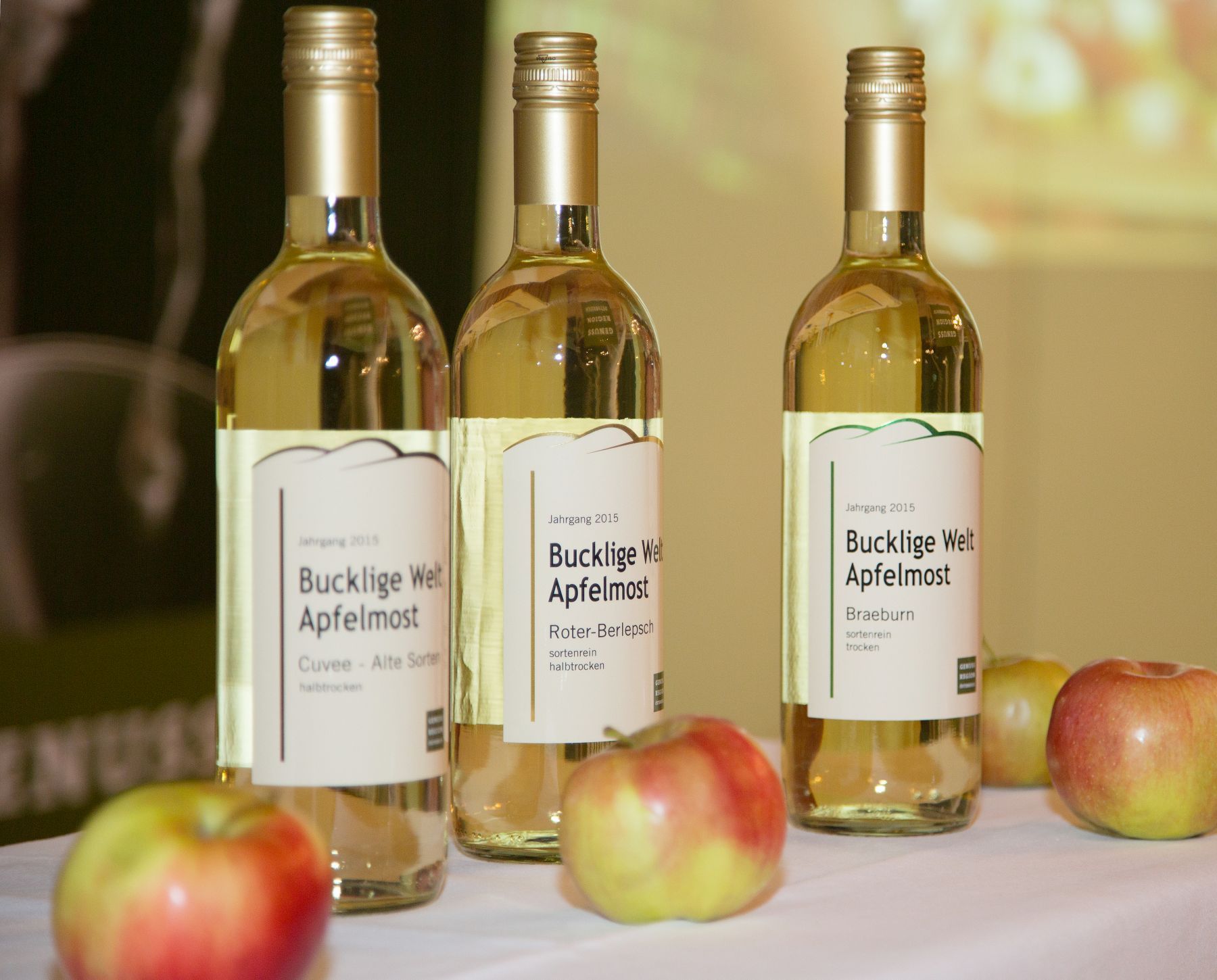 Three bottles of Bucklige Welt cider on a table with apples.