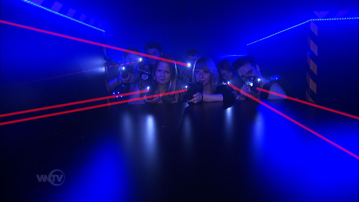 People play laser tag in a dark room with blue lights and red laser beams.