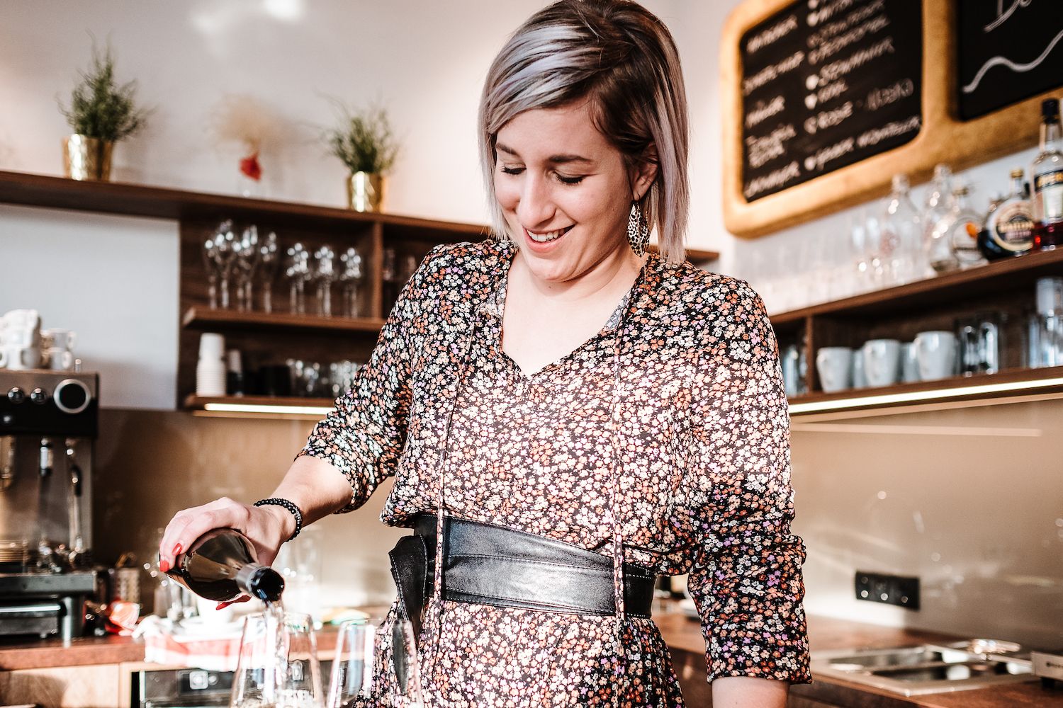 Woman in flowered dress pouring drink in a café.
