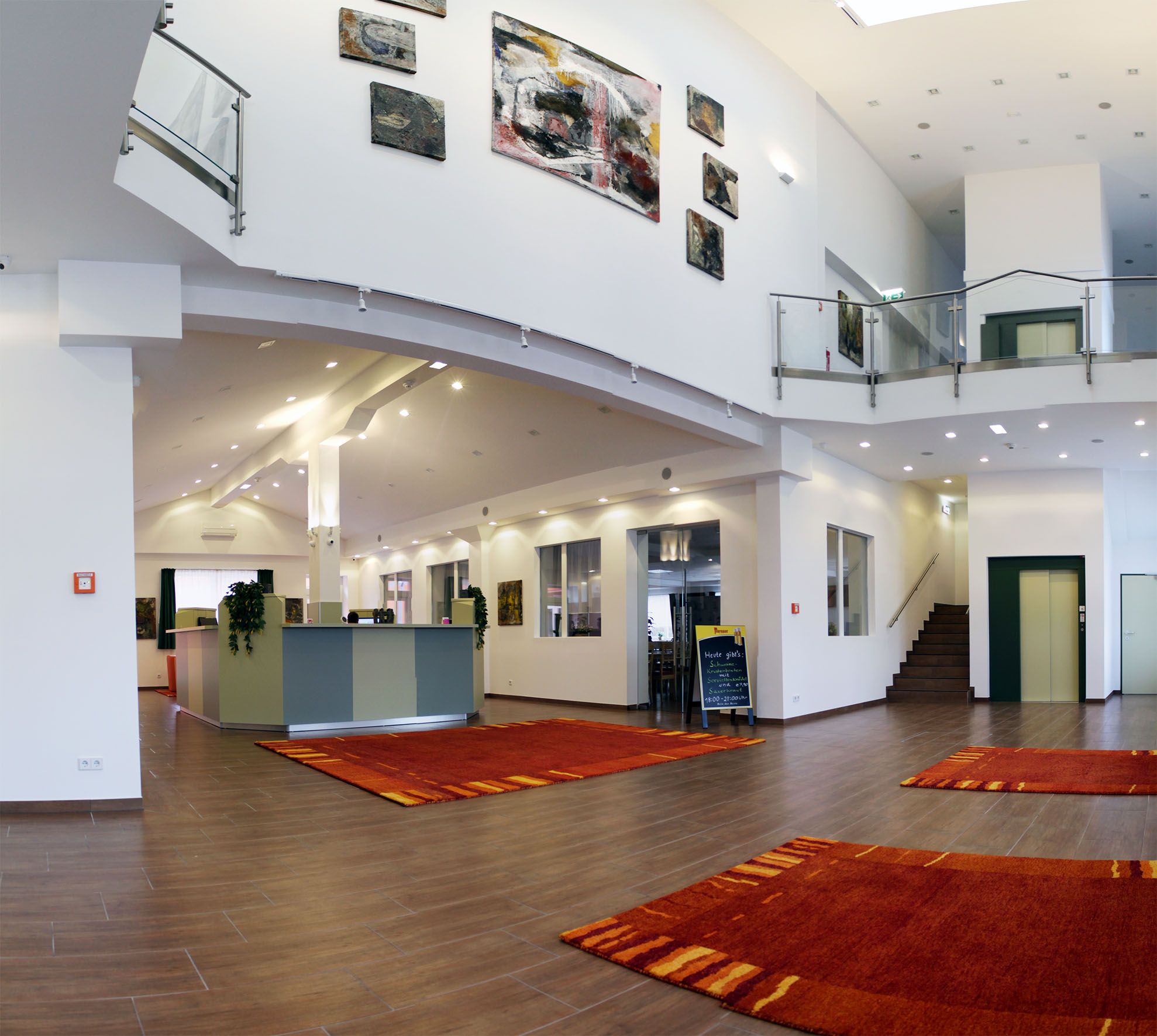 Modern hotel lobby with reception, red carpets and works of art on the walls.