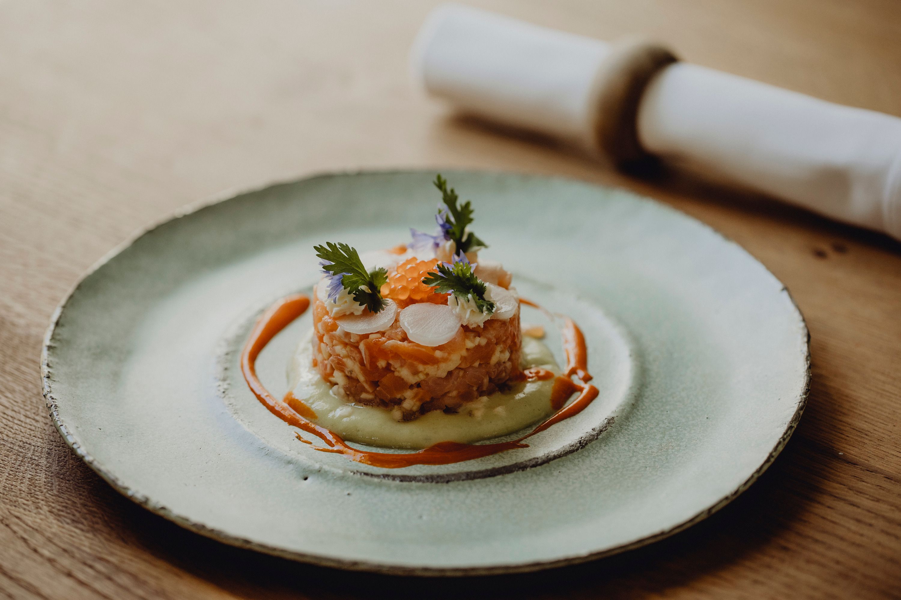Gourmet dish on a plate decorated with salmon, herbs and sauce.