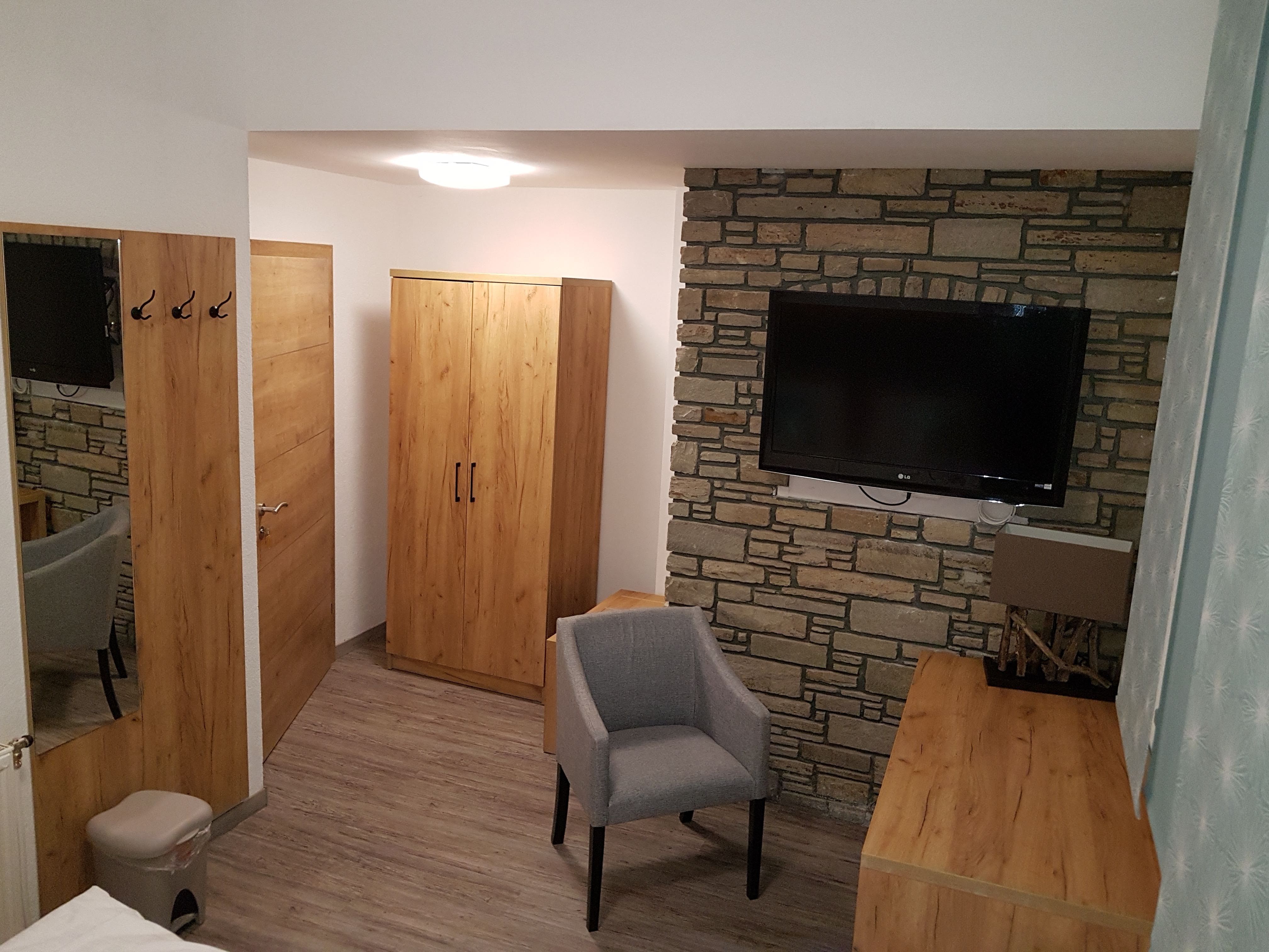 Hotel room with wooden furniture, gray armchair and flat screen TV on a stone wall.