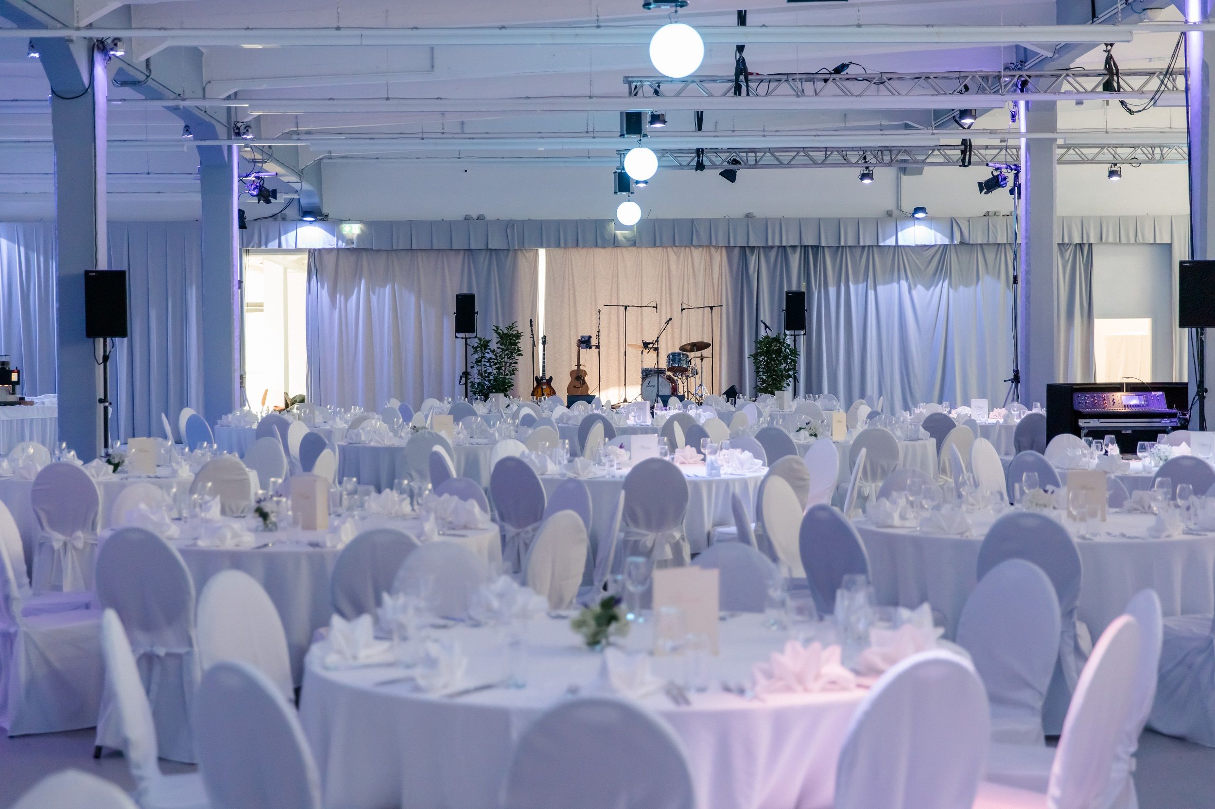 Elegant function room with round tables set in white and a stage with musical instruments.