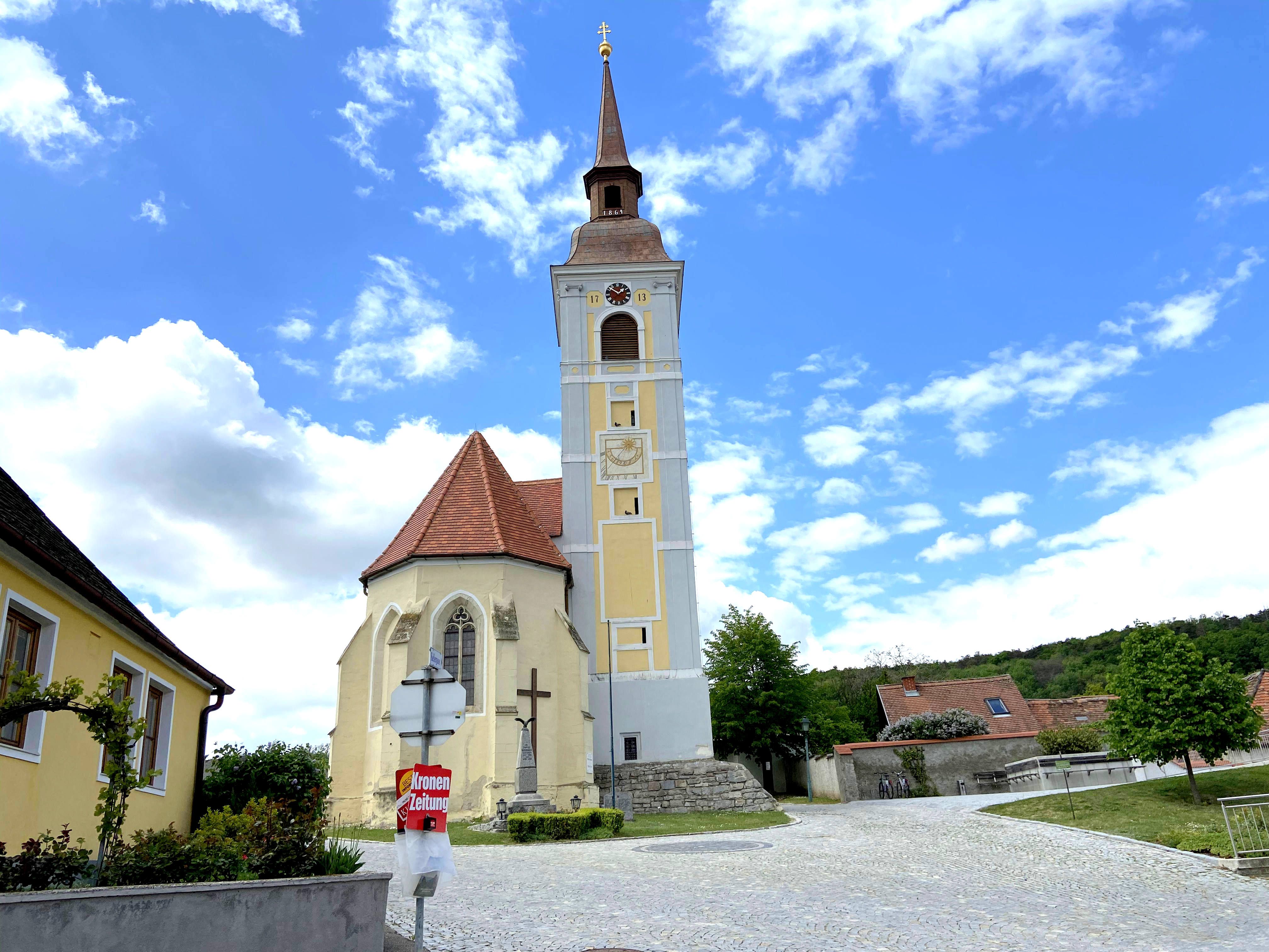 Church with leaning tower in Waitzendorf, surrounded by blue sky and clouds.