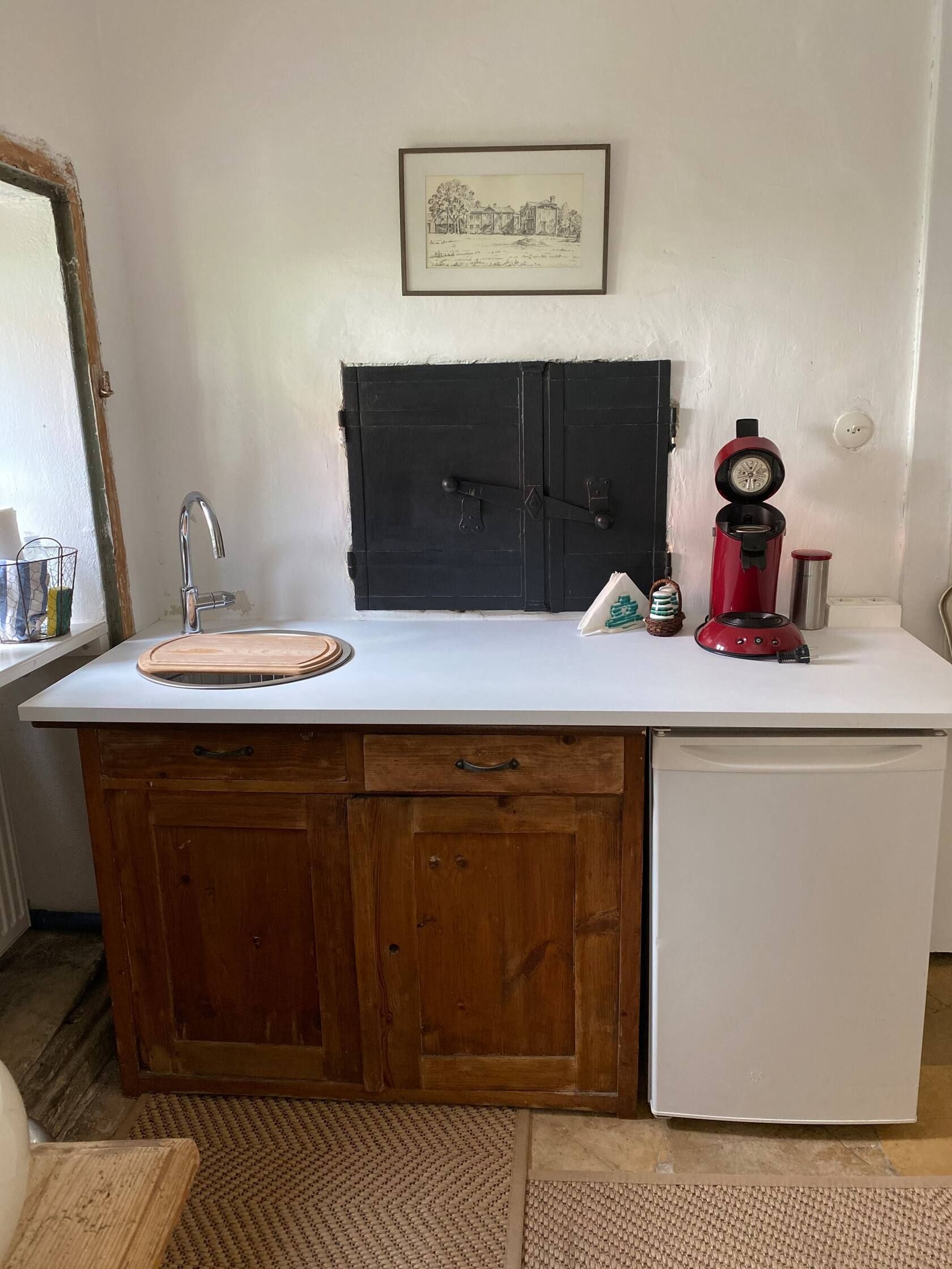 Small kitchen with wooden cupboards, white worktop, red coffee machine and small fridge.