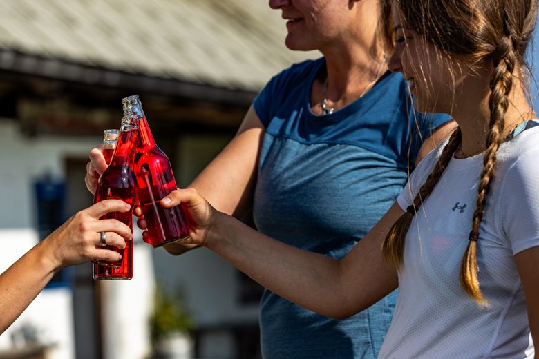 Three people clink glasses with red drinks bottles.