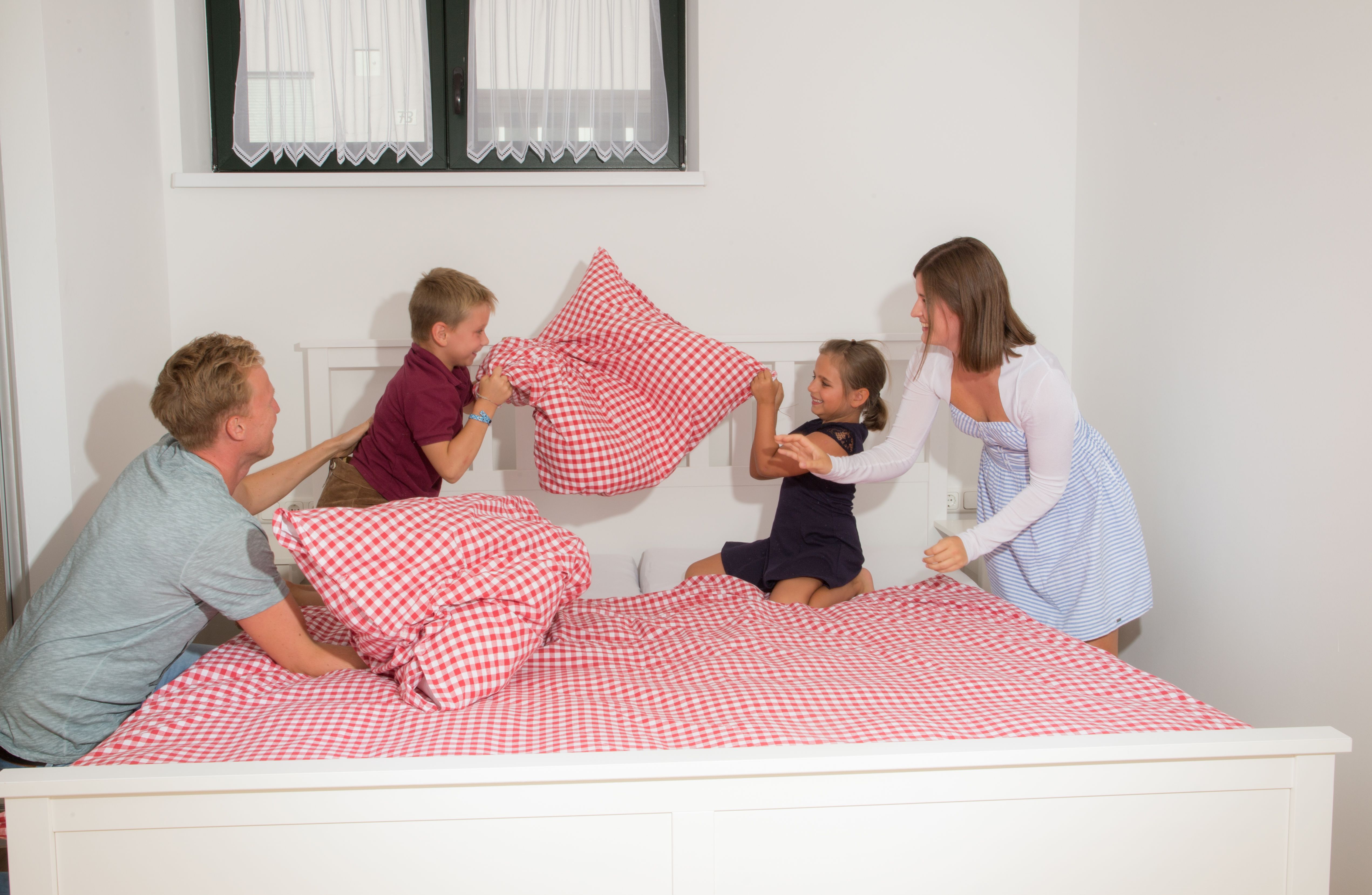 Family having pillow fight on a bed with red and white checkered bedding.