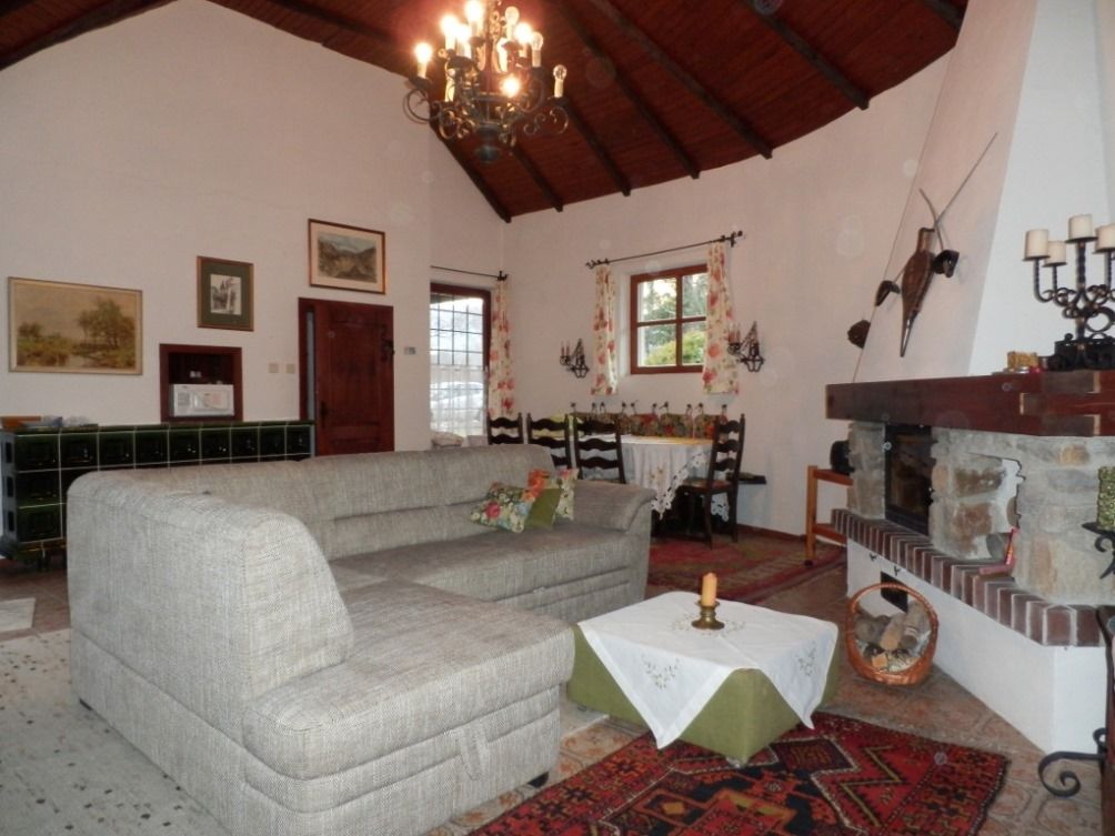Cozy living room with grey sofa, fireplace and dining table. Rustic decoration and wooden beamed ceiling.
