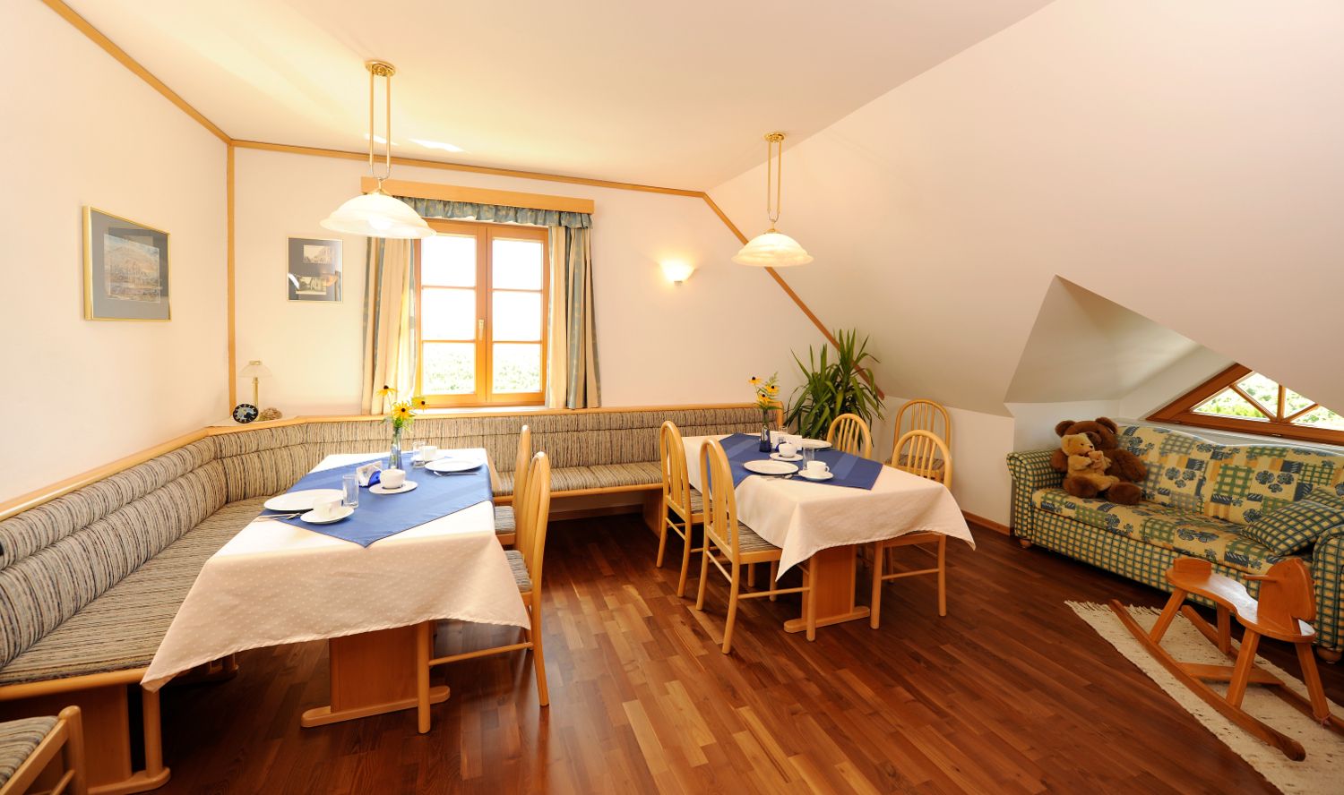 Cozy breakfast area with wooden furniture, laid tables and a sofa with teddy bears.