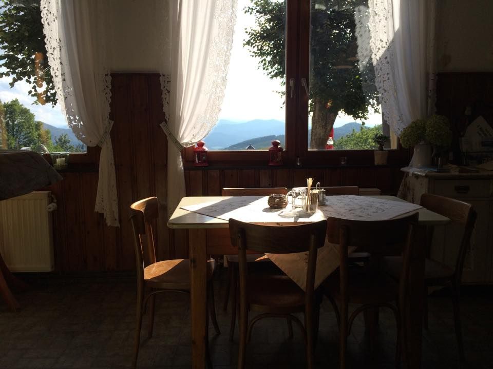 A cozy dining area with a wooden table and chairs in front of a large window with a view of the mountains and trees.