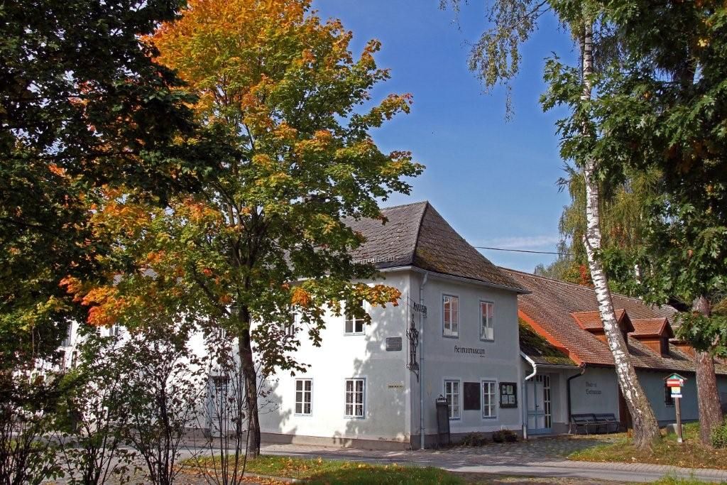 A white building with the inscription 'Heimatmuseum', surrounded by trees with autumn leaves.