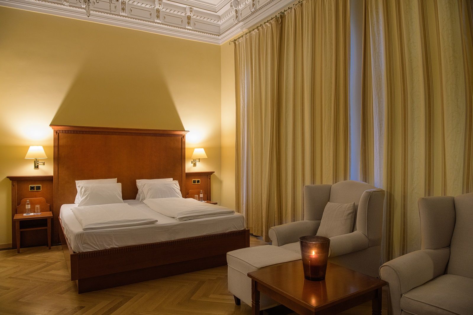 Elegant double room with a large bed, two armchairs and a table with a candle.
