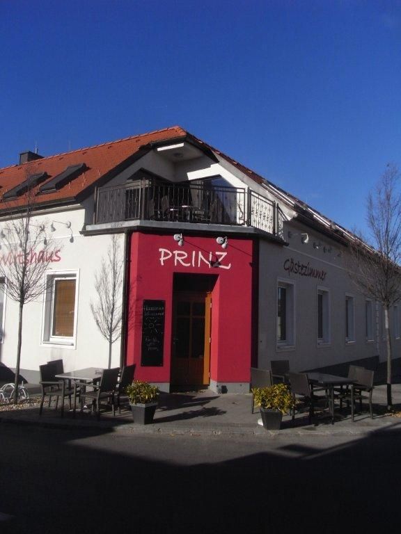 Exterior view of a building with the inscription 'Prinz', guest garden with tables and chairs, blue sky.
