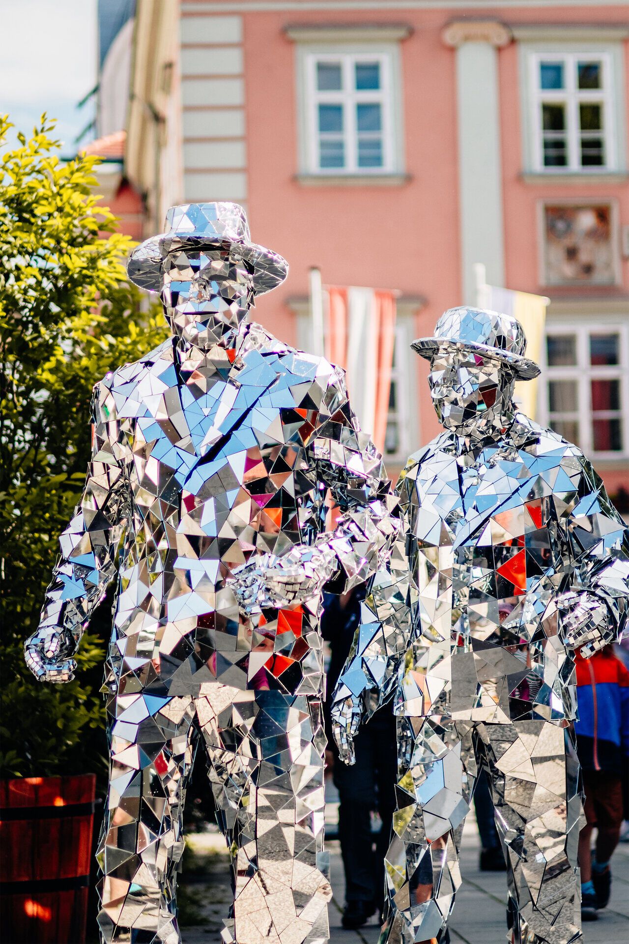 Zwei Straßenkünstler in verspiegelten Kostümen und Hüten gehen Hand in Hand durch die Innenstadt von Wiener Neustadt beim Straßenkunstfestival.
