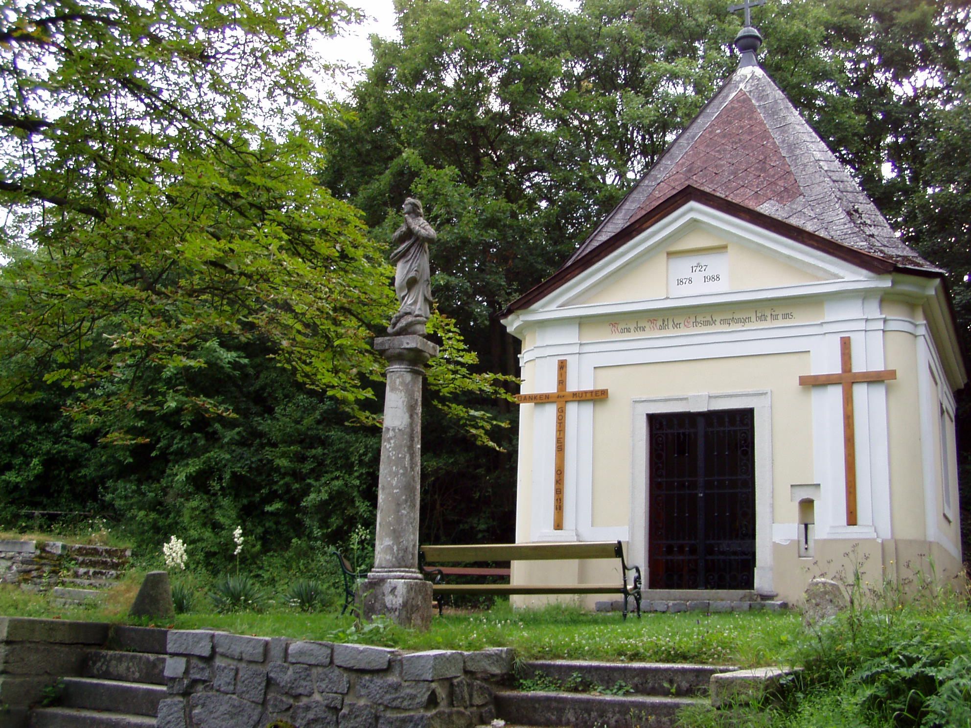 Chapel with statue and cross in a green park.