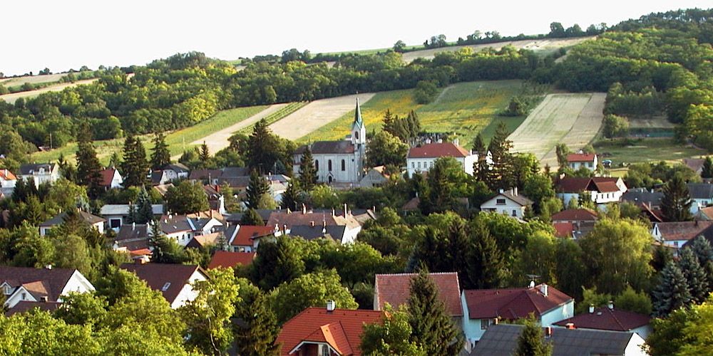 Panorama of Unterolberndorf with church and surrounding houses in front of green hills.