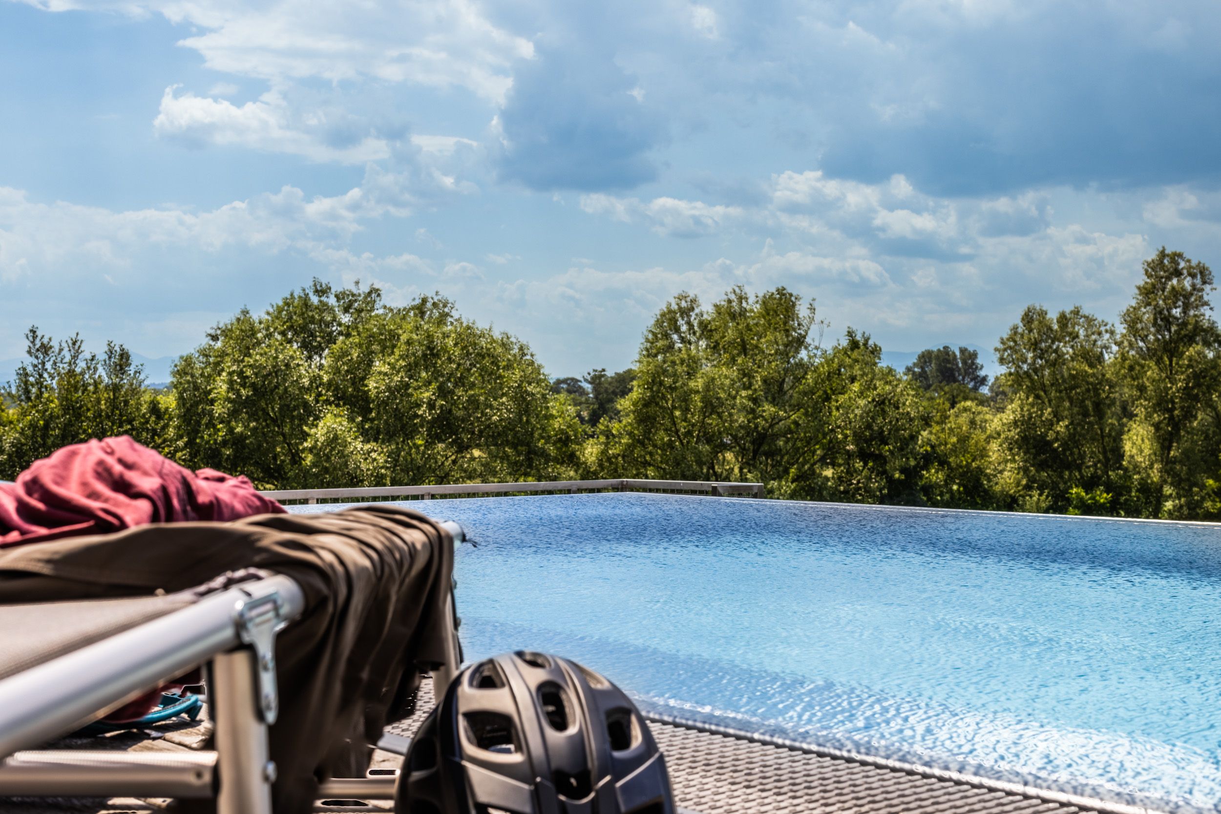 An infinity pool with trees in the background and a bicycle helmet in the foreground.