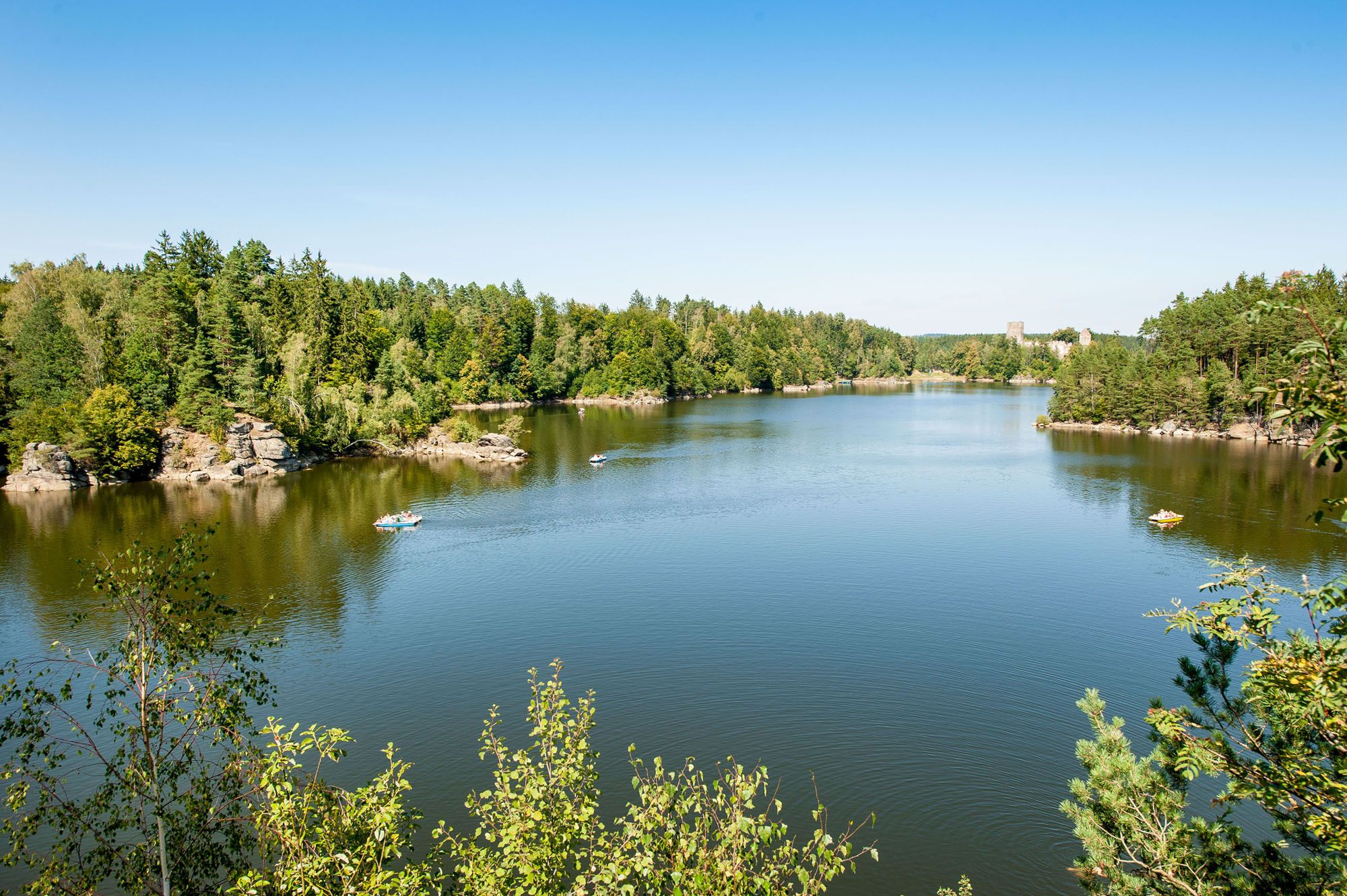 A peaceful lake with surrounding woods and several boats on the water.