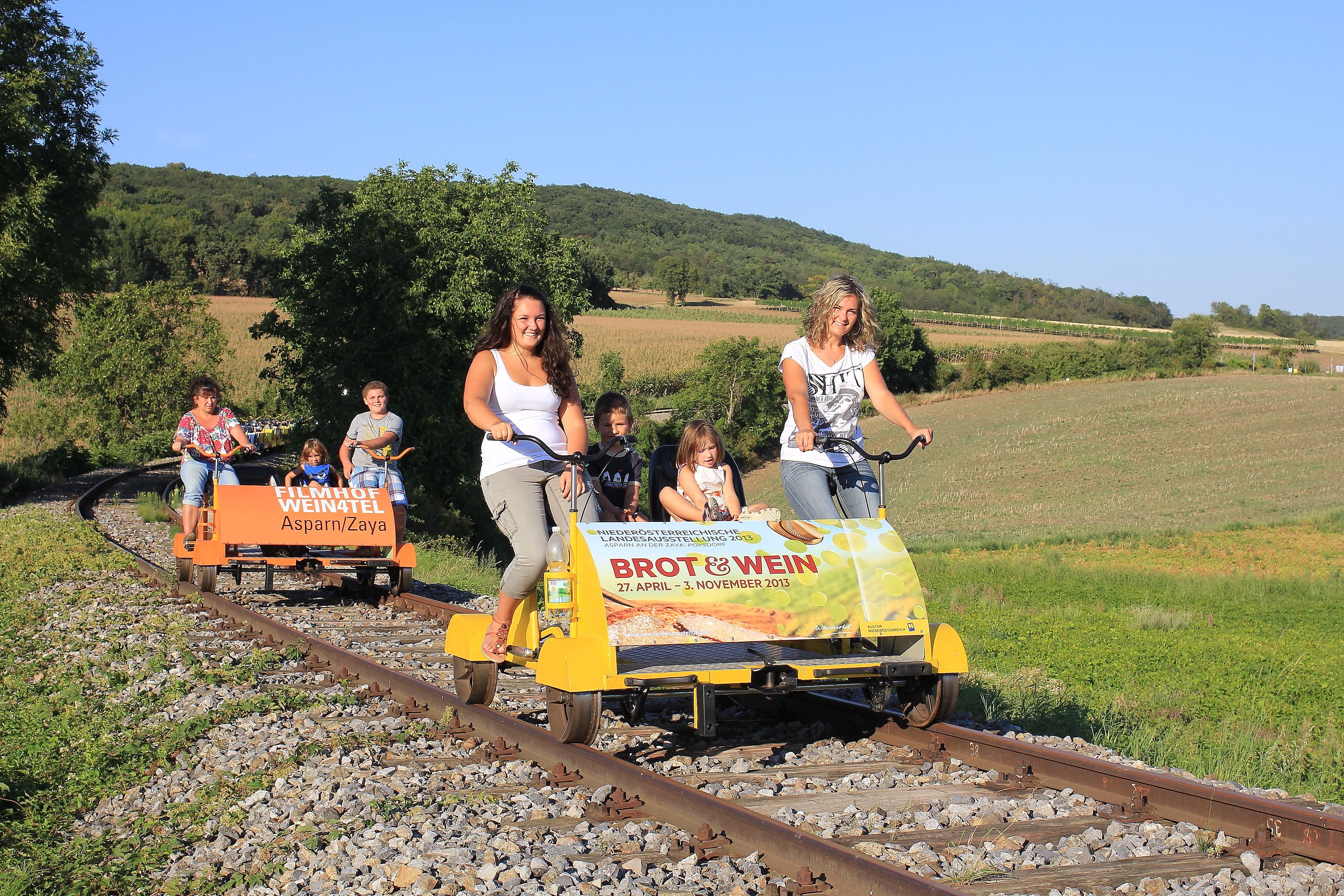 People ride on trolleys through a rural landscape.