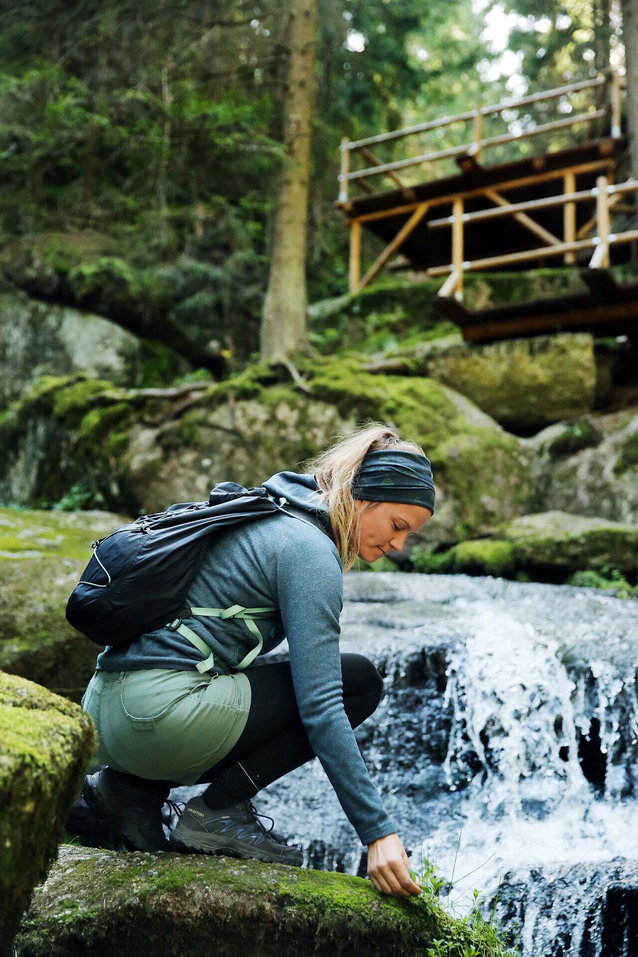In the midst of lush nature, a hiker kneels on the bank of a babbling brook and admires the fresh, green surroundings. The gentle waterfalls in the background lend the scenery a magical atmosphere that invites you to linger. Here, where the tranquillity of nature meets the beauty of water, every moment becomes an unforgettable experience.