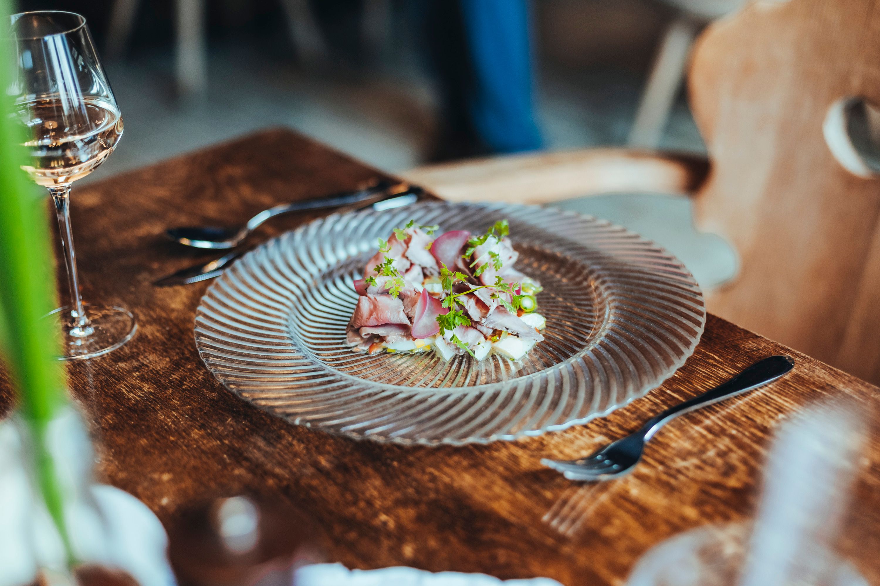 A plate of roast beef and asparagus salad on a wooden table, with a glass of white wine next to it.