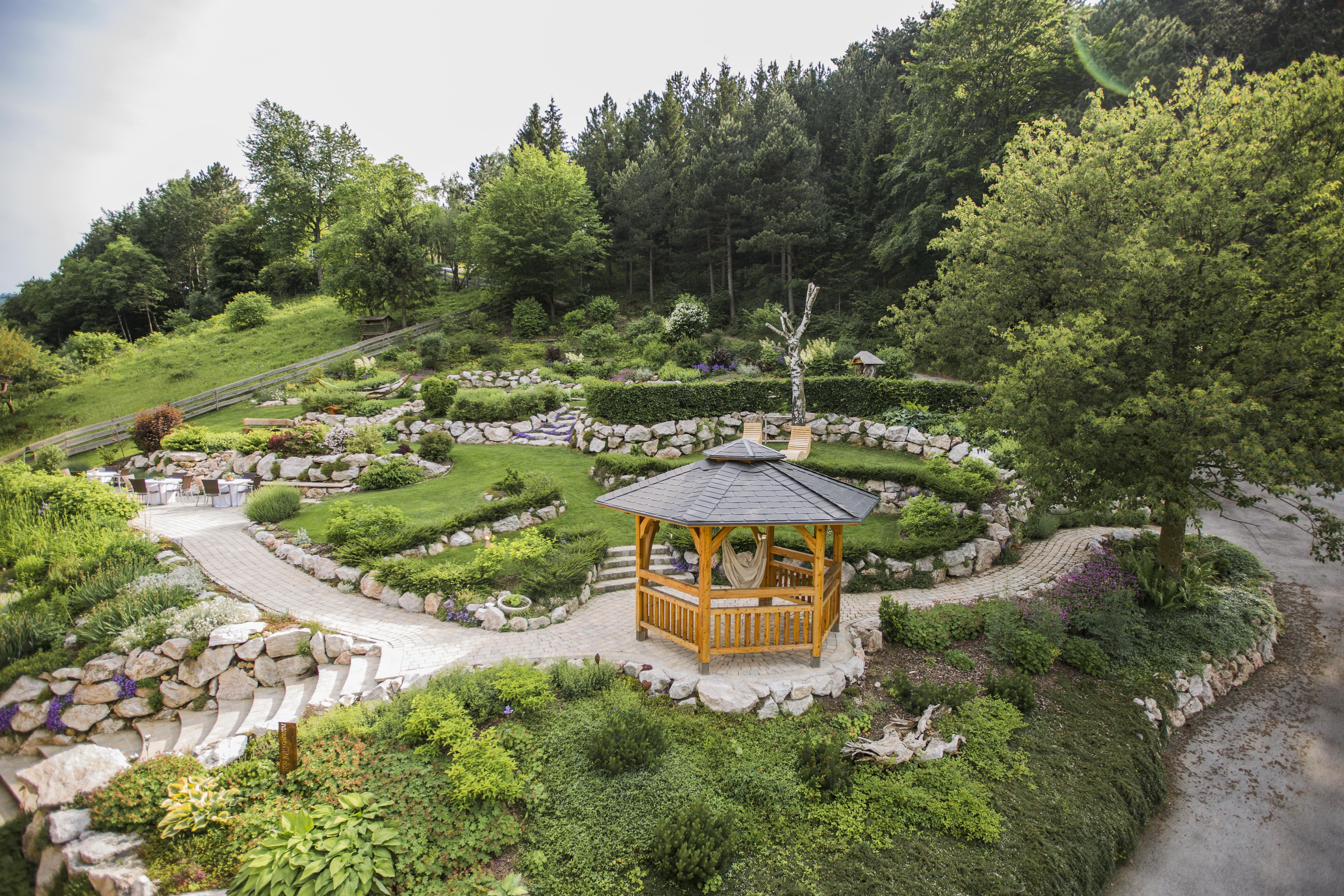 A wooden pavilion in a well-tended garden with green trees and stone paths.