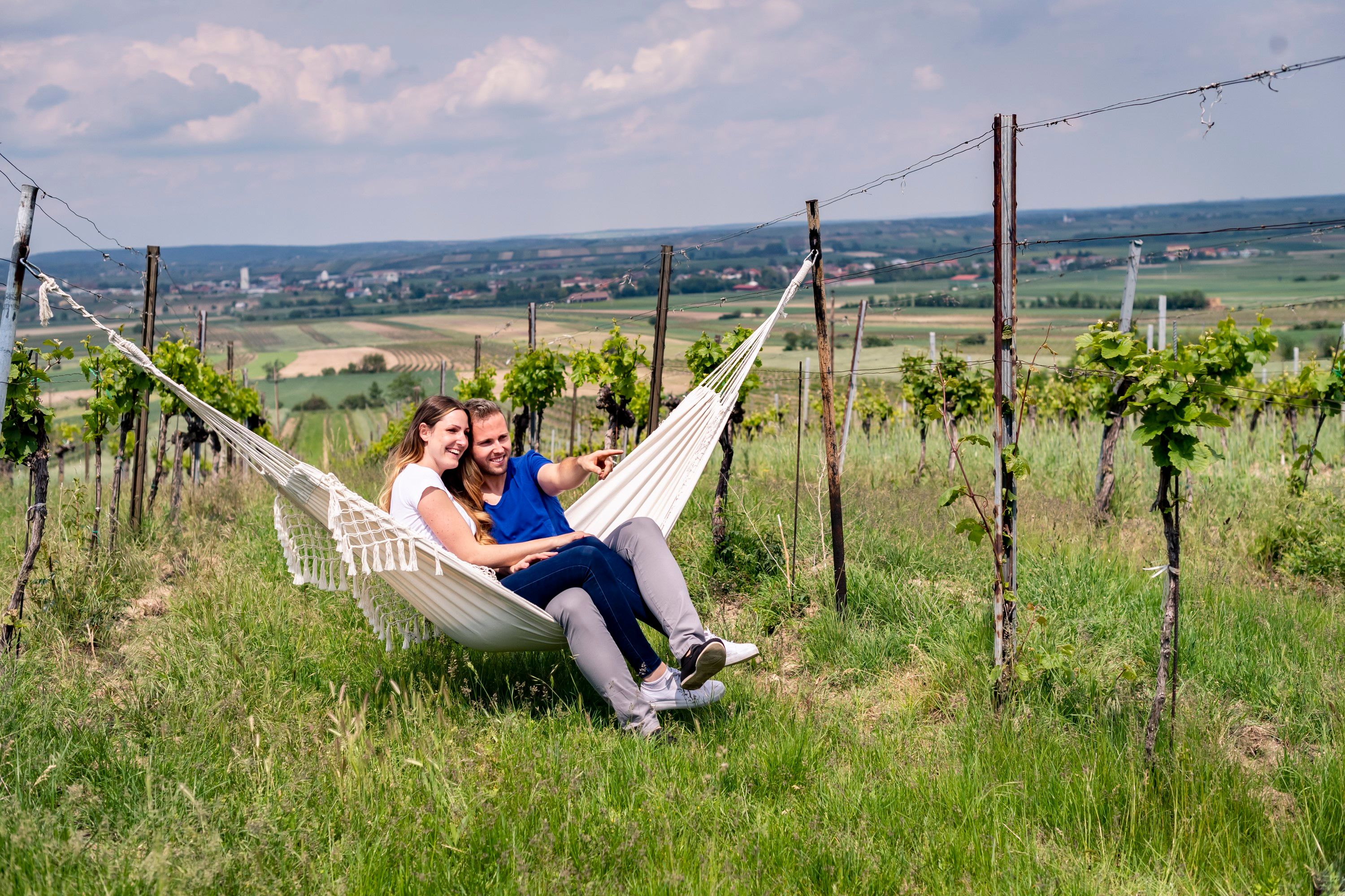 A couple sits in a hammock in a vineyard and enjoys the view of the landscape.