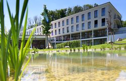 A modern building with a terrace in a green park with flowers and trees.