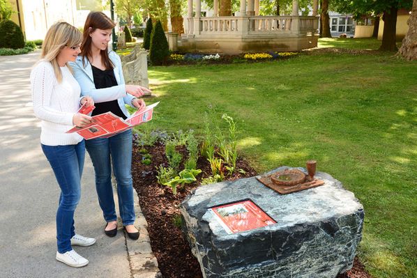 Two women look at information material on a stone with a memorial plaque outside.