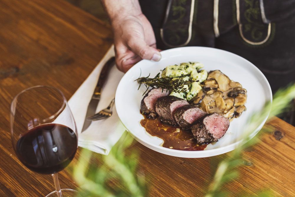 A plate of meat, mushrooms and spaetzle, with a glass of red wine next to it.