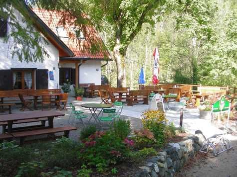Outdoor area of the Schindlhütte with tables and chairs in the green.