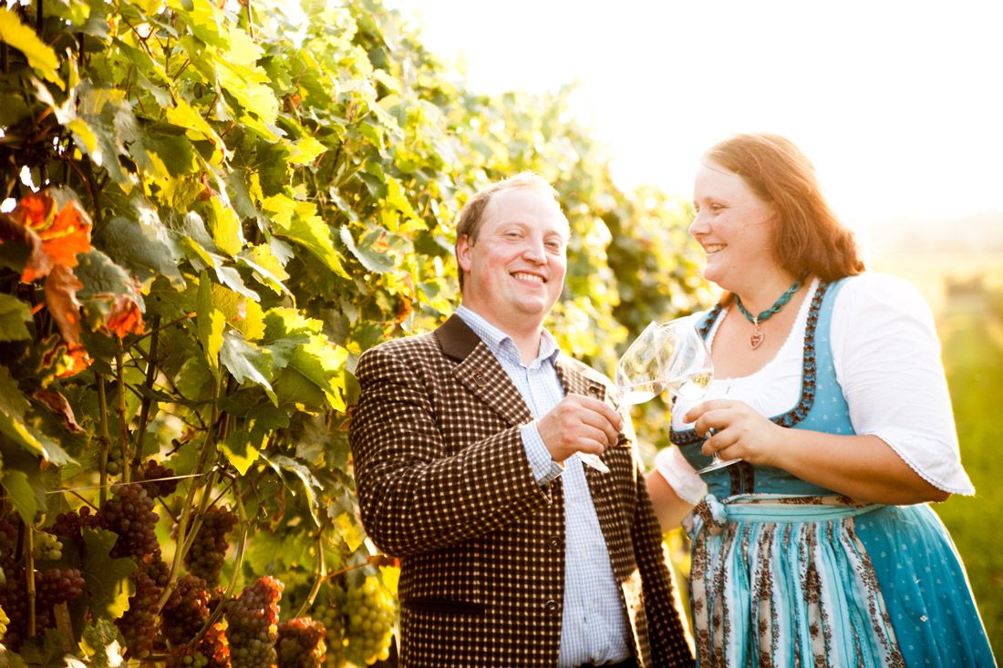 A man and a woman clink glasses in a vineyard.