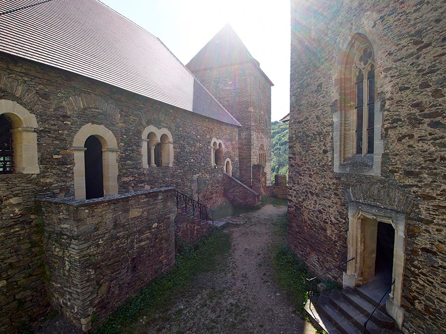 Inner courtyard of Hardegg Castle with old stone walls and Gothic windows, rays of sunshine in the background.