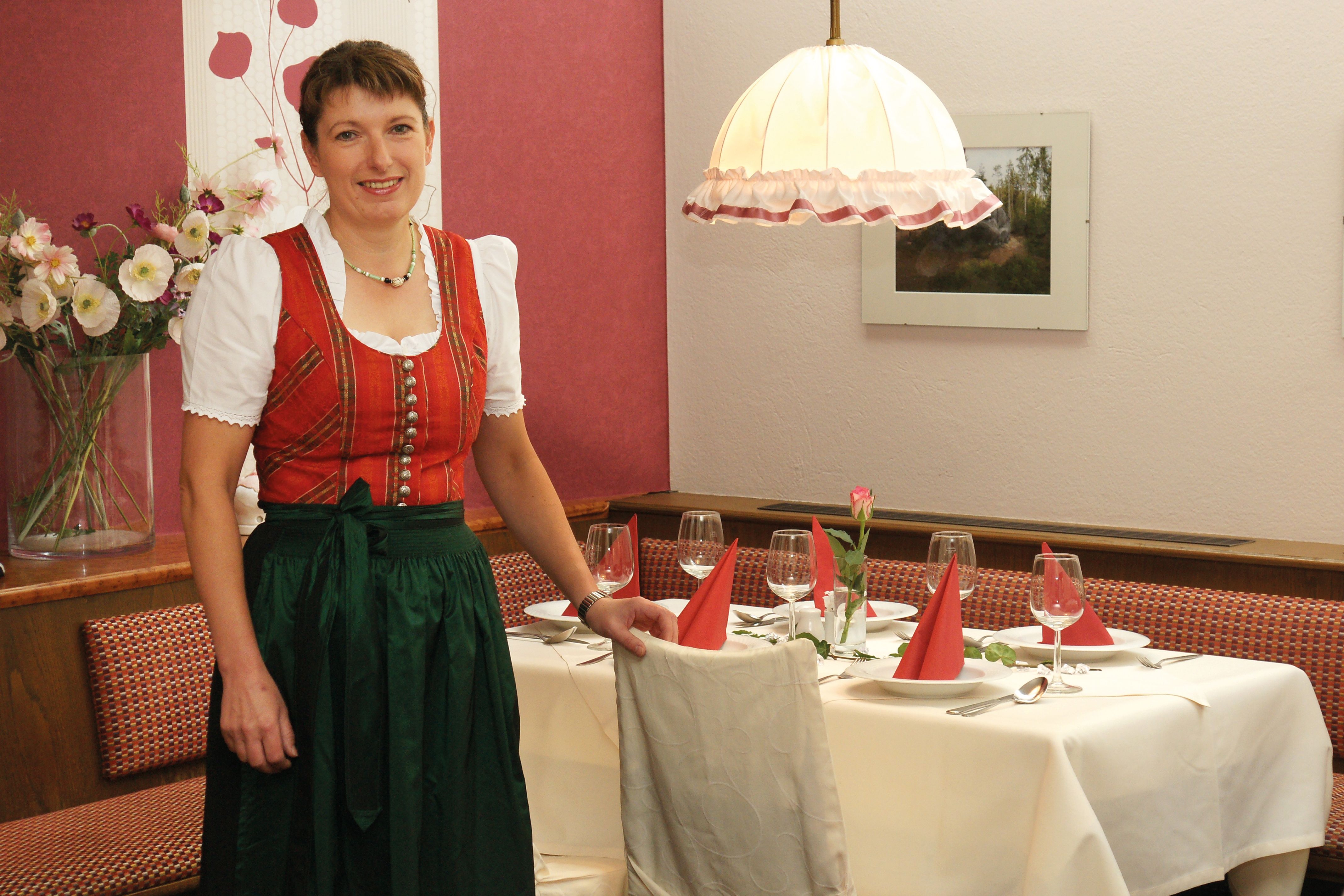 A woman in traditional dress stands next to a laid table in a restaurant.