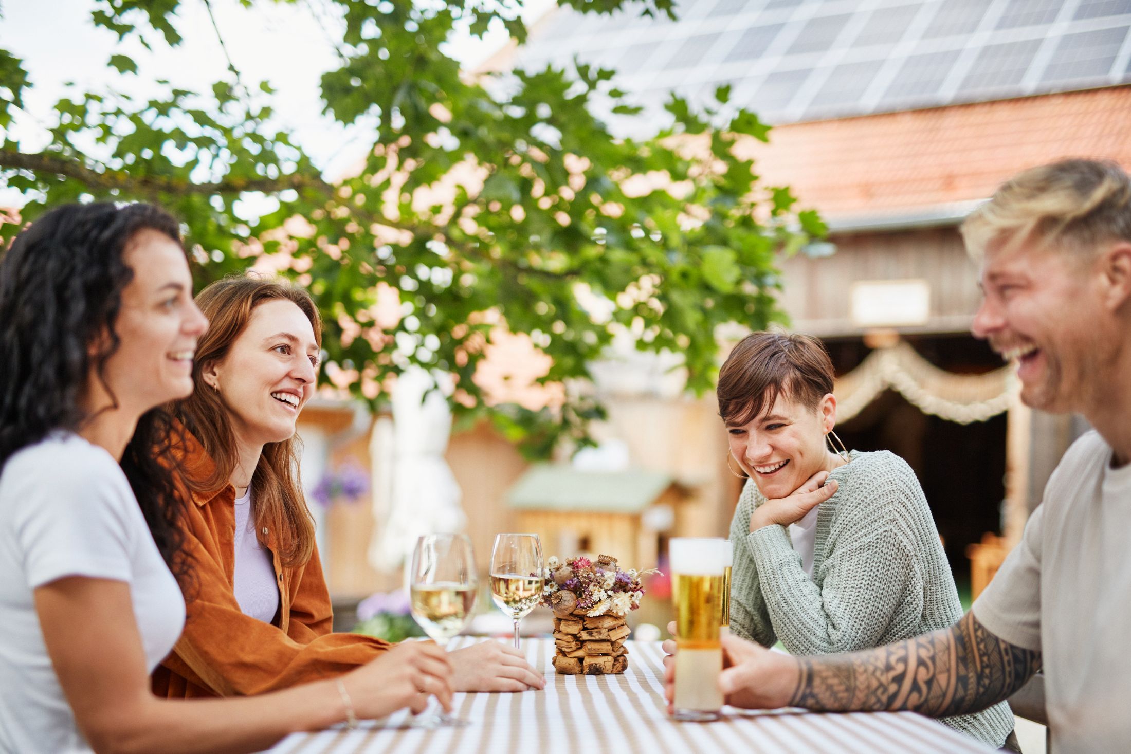 Four people sit laughing at an outdoor table with drinks.