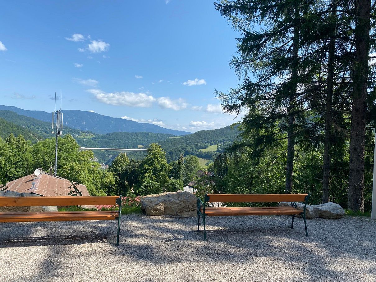 Two benches with a view of a mountain landscape and a bridge.