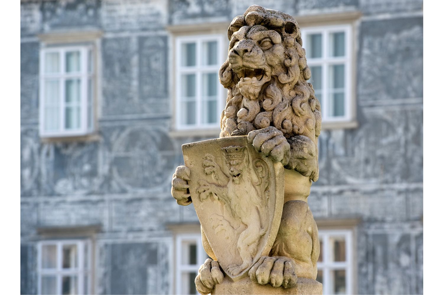 Stone lion with coat of arms on a fountain in front of a building.