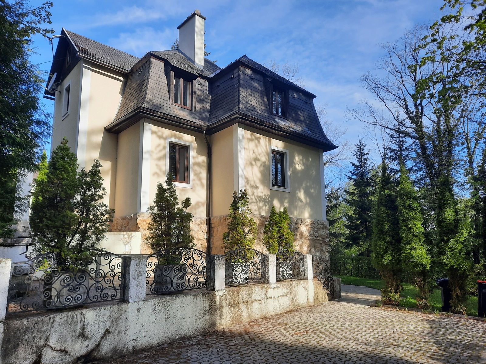 A two-storey villa with a mansard roof, surrounded by trees and a wrought-iron fence.