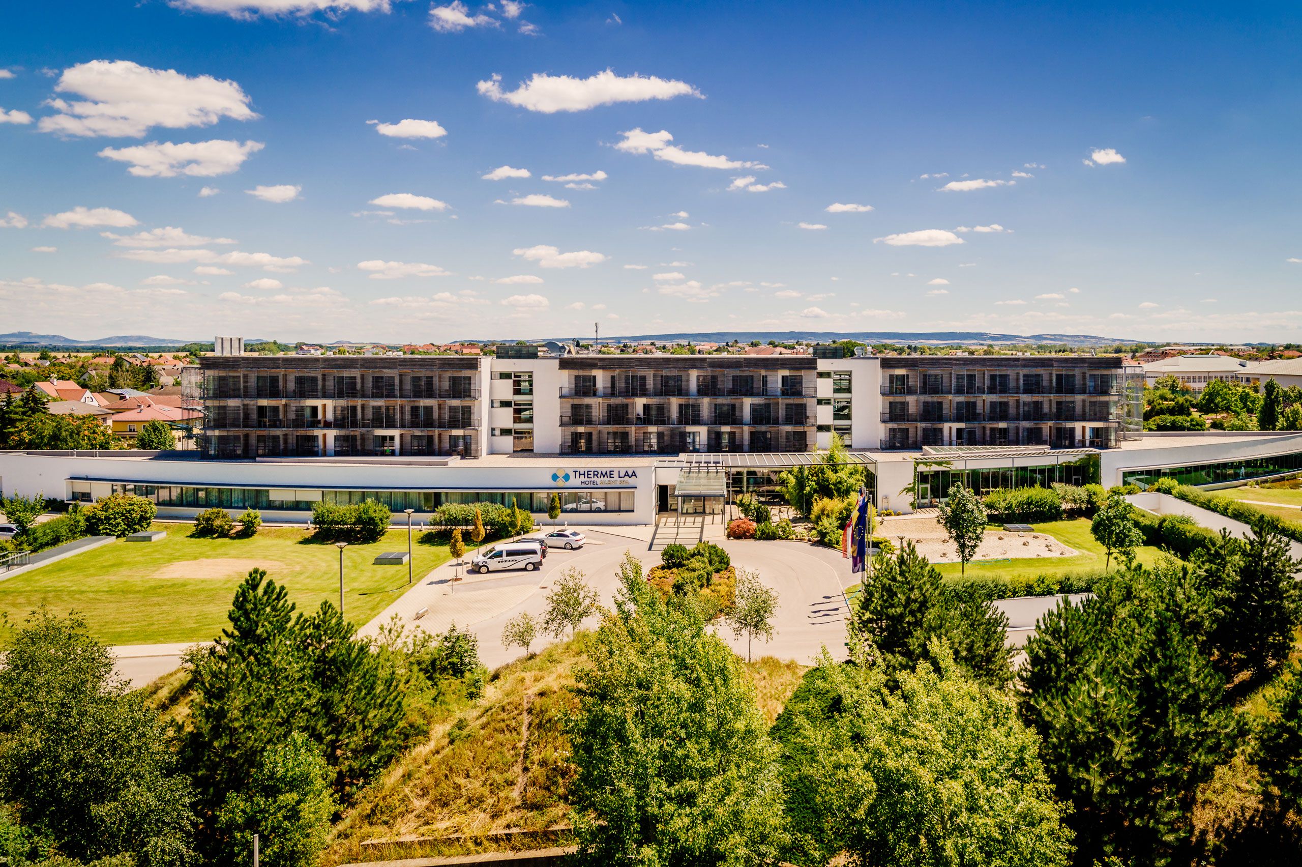 Exterior view of the Therme Laa Hotel with green garden and blue sky.