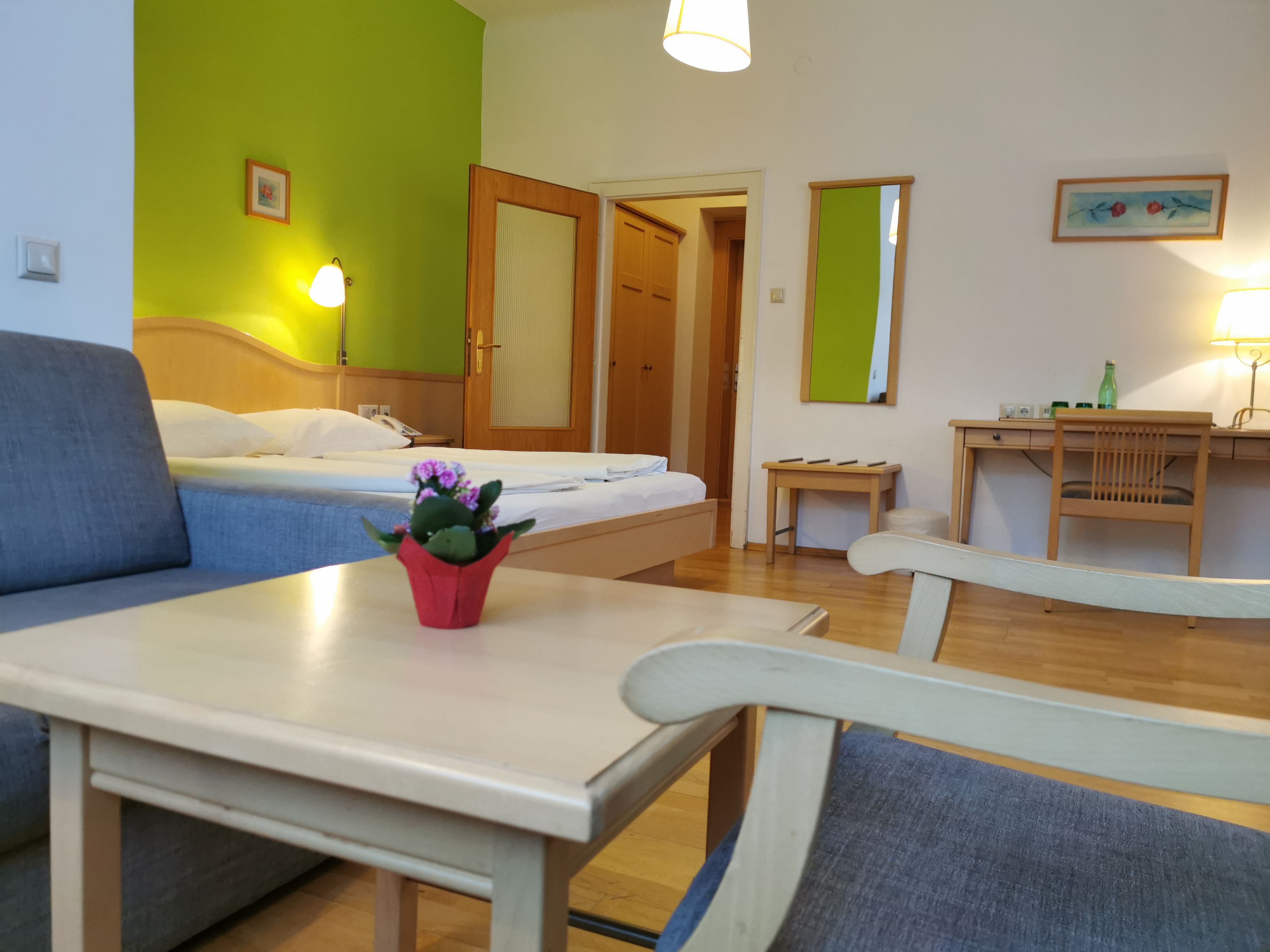 Hotel room with green accent, bed, desk and armchair.