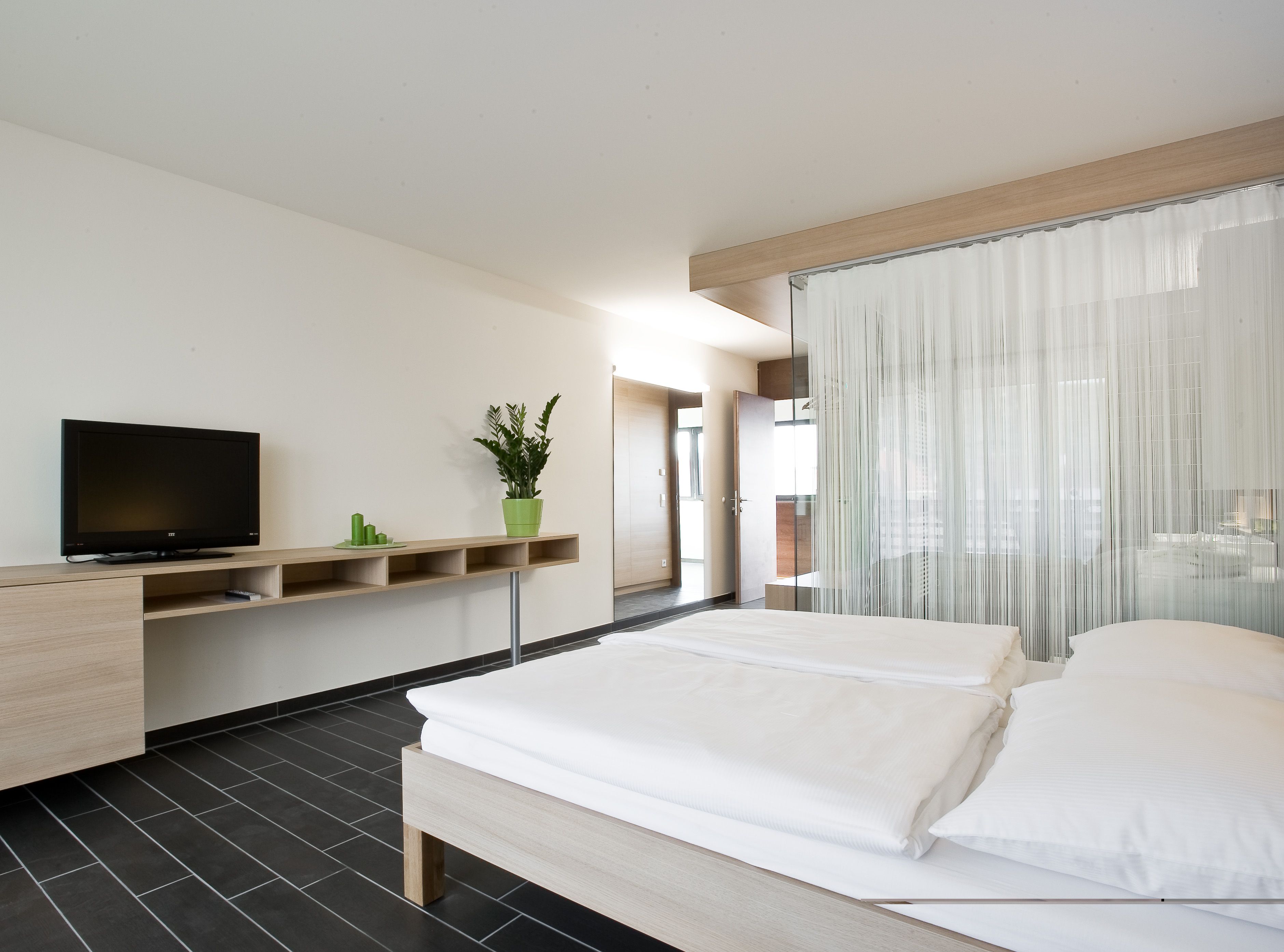 Modern hotel room with double bed, TV and plants.