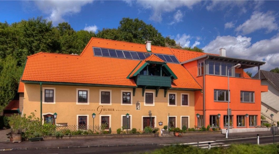A traditional inn with an orange roof and solar panels, surrounded by green nature.