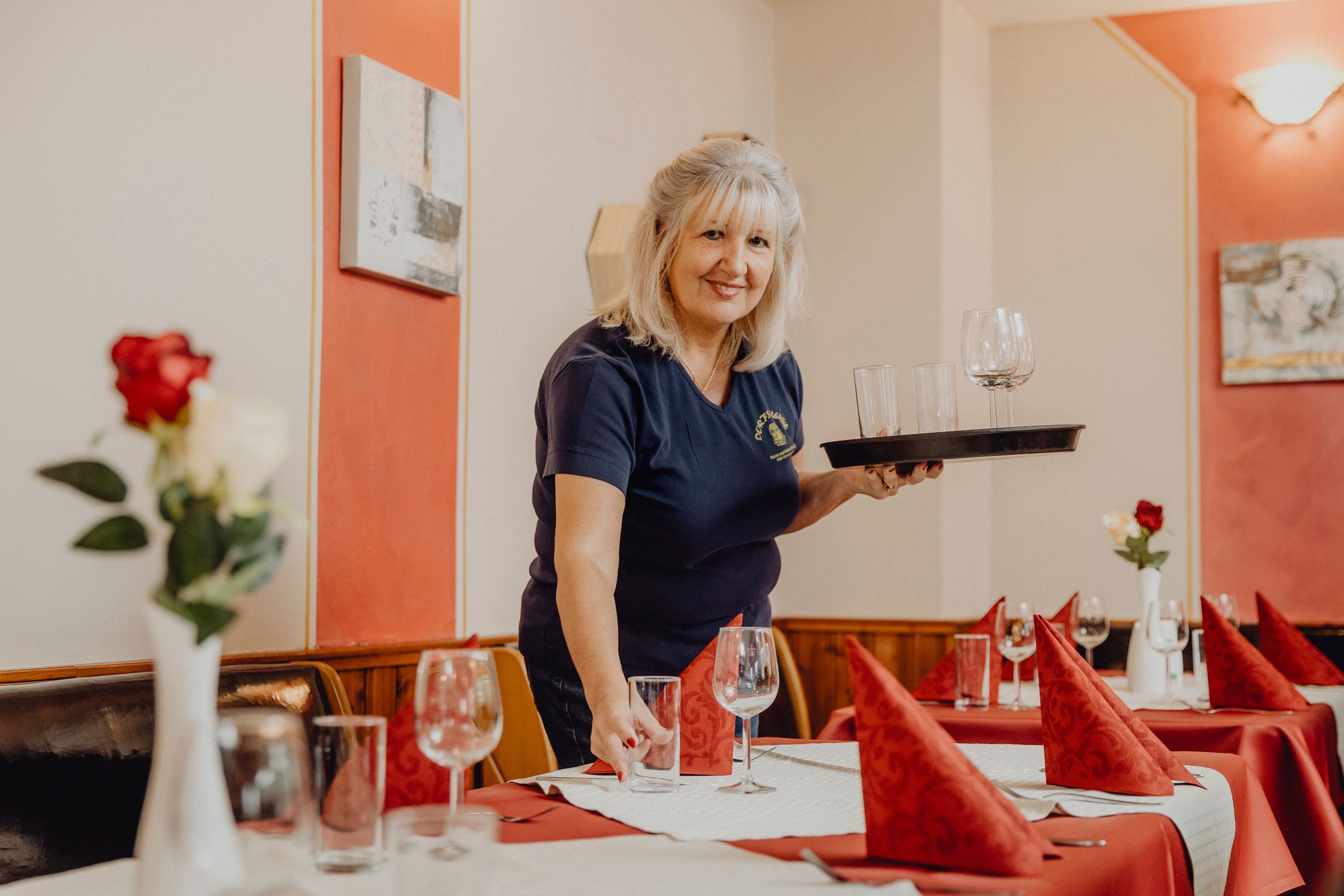 Woman sets table in a restaurant with glasses and red napkins.