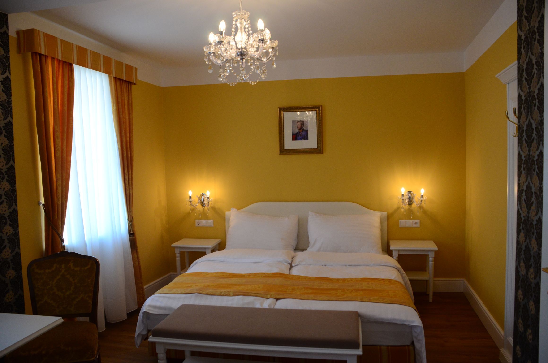Elegant hotel room with yellow walls, double bed, chandelier and picture on the wall.