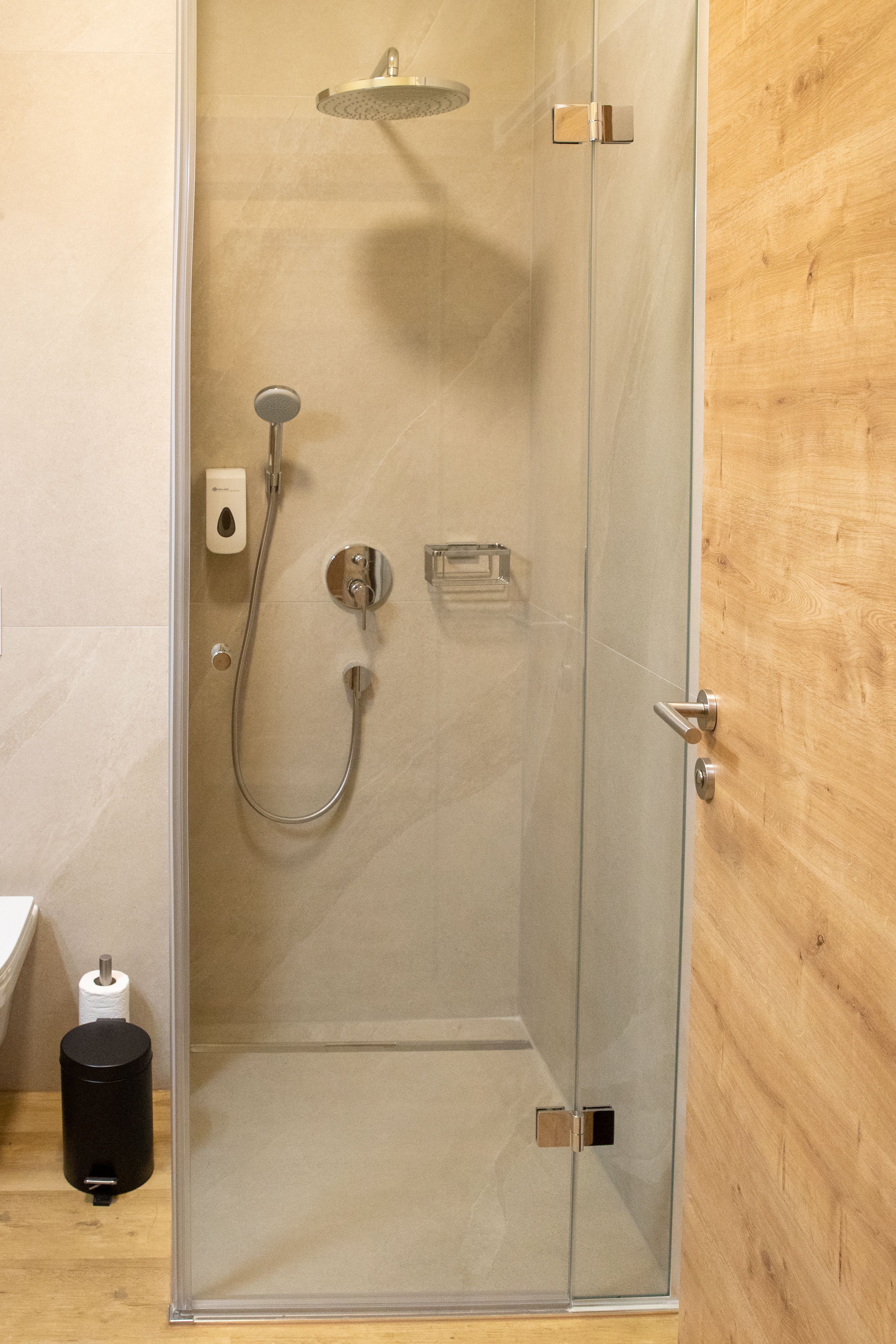 Modern bathroom with glass shower, shower head and wooden details.